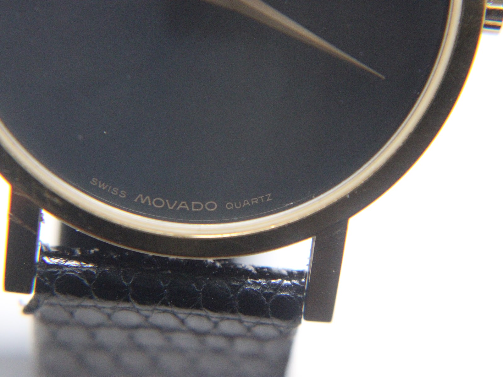 Close-up of the bottom of the black dial, showing 'SWISS MOVADO QUARTZ' text and the edge of the gold-plated case.