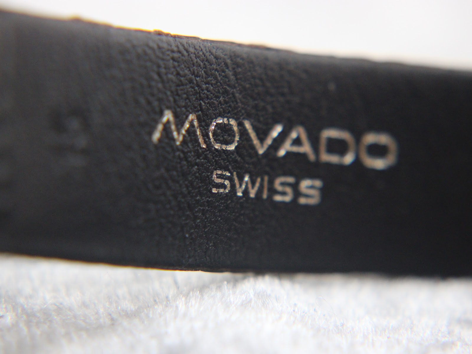 Close-up of 'Movado Swiss' branding embossed on the black textured leather strap.