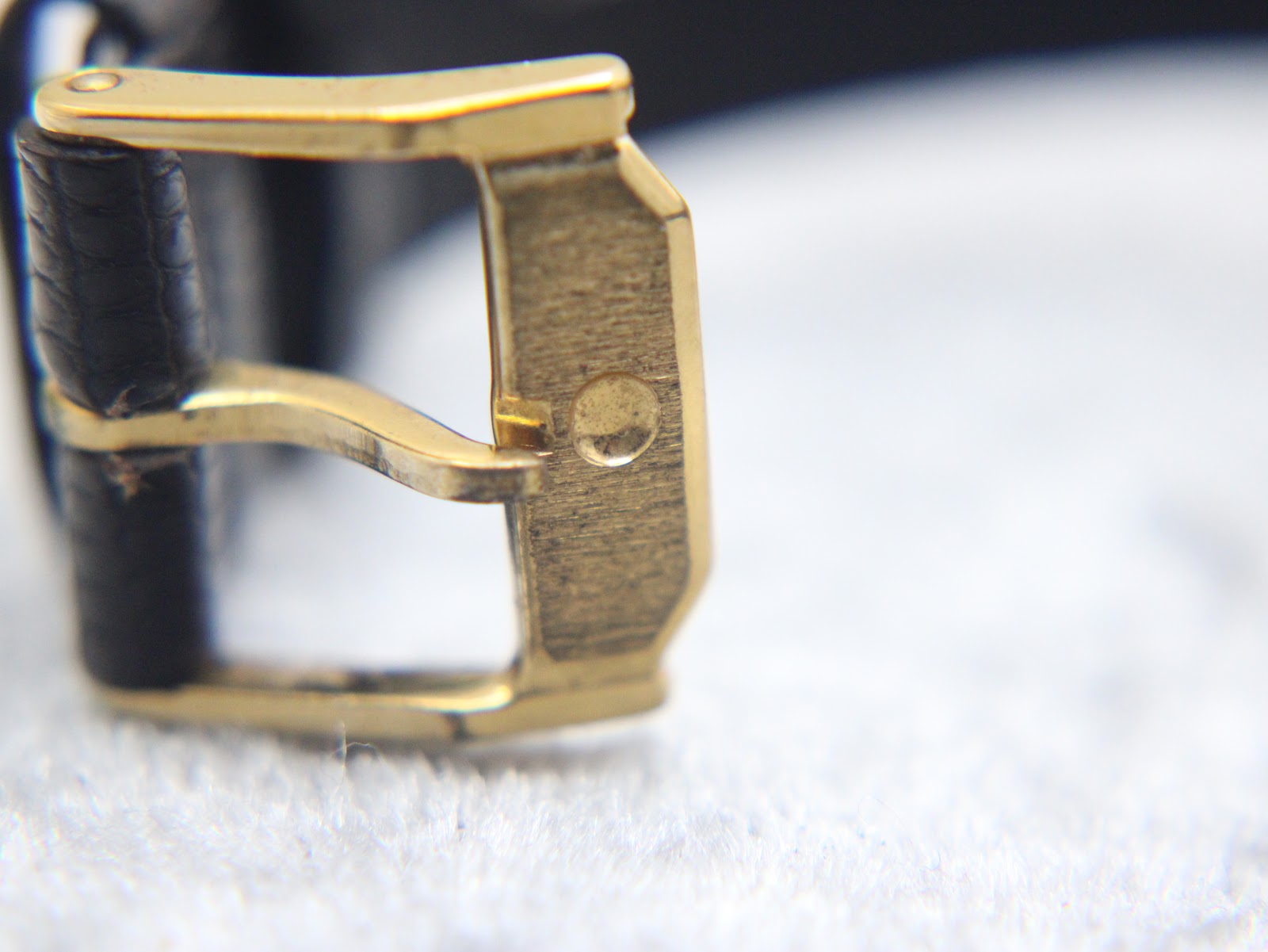 Macro shot of the original gold-tone Movado branded buckle with a brushed finish.
