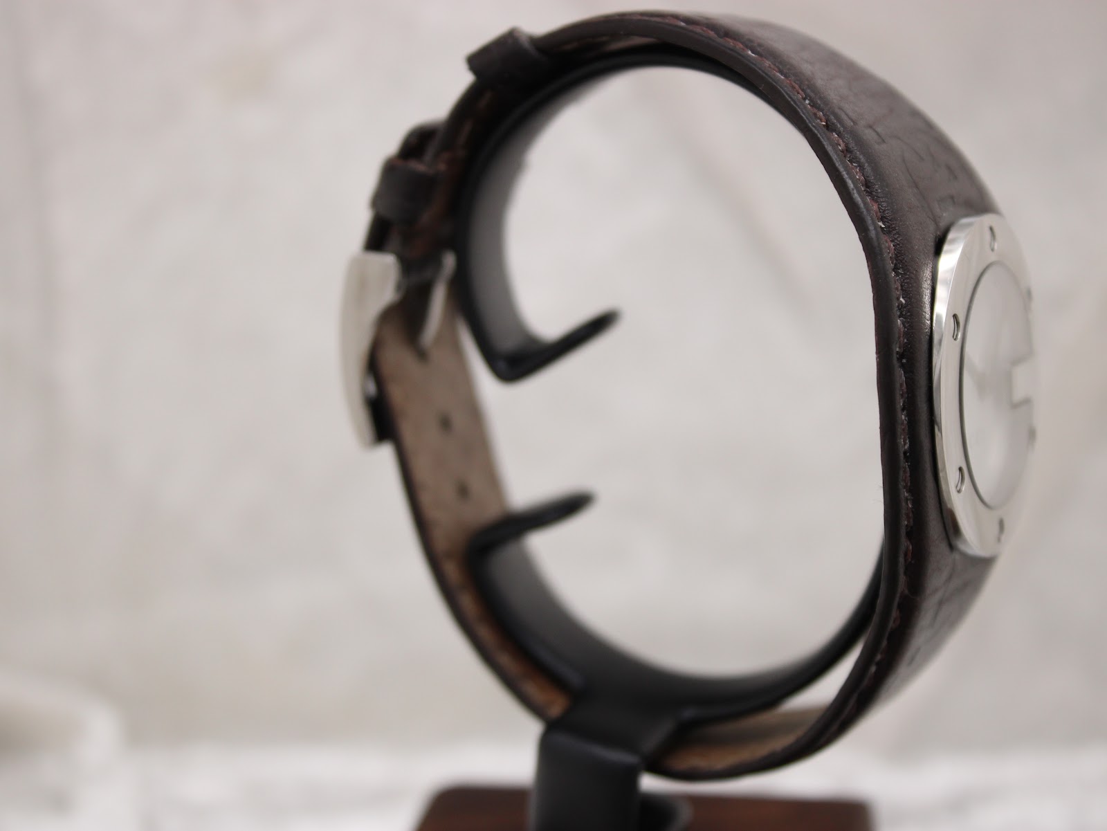 Alternate side view of the Gucci 104 watch on a stand, showing the other side of the stainless steel case and brown leather strap.