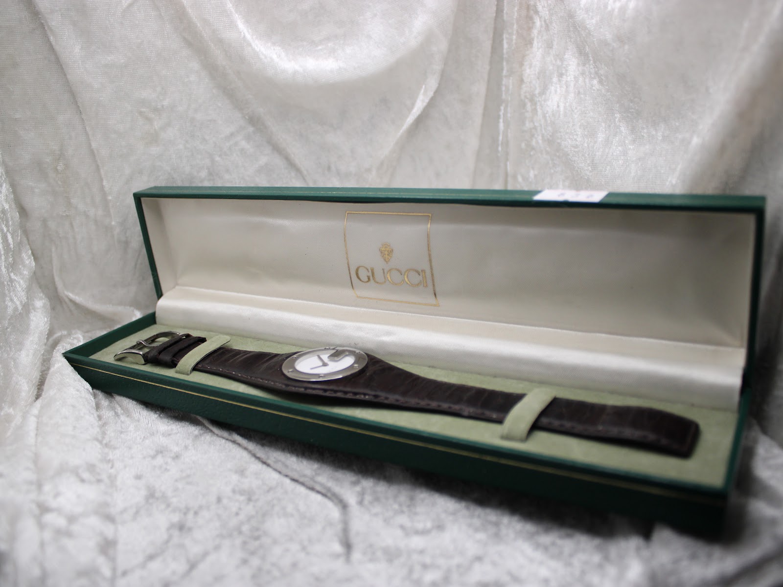 Gucci 104 watch in its open, original dark green presentation box with golden Gucci logo inside.