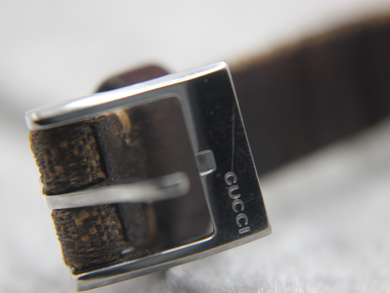 Close-up of the polished stainless steel buckle, with 'GUCCI' clearly engraved on the side.
