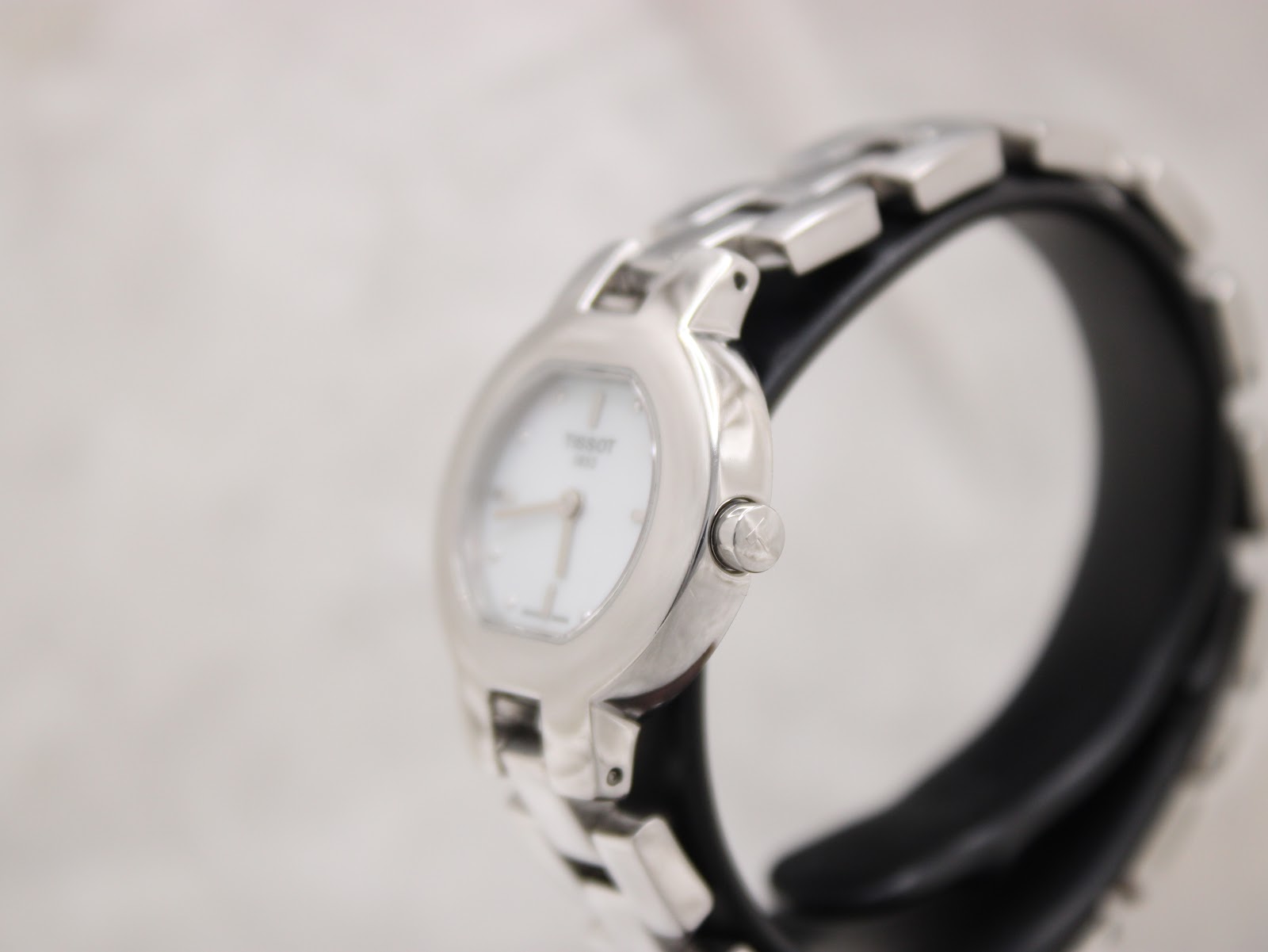 Side view of the Tissot watch on a stand, showing the signed crown and curved case.