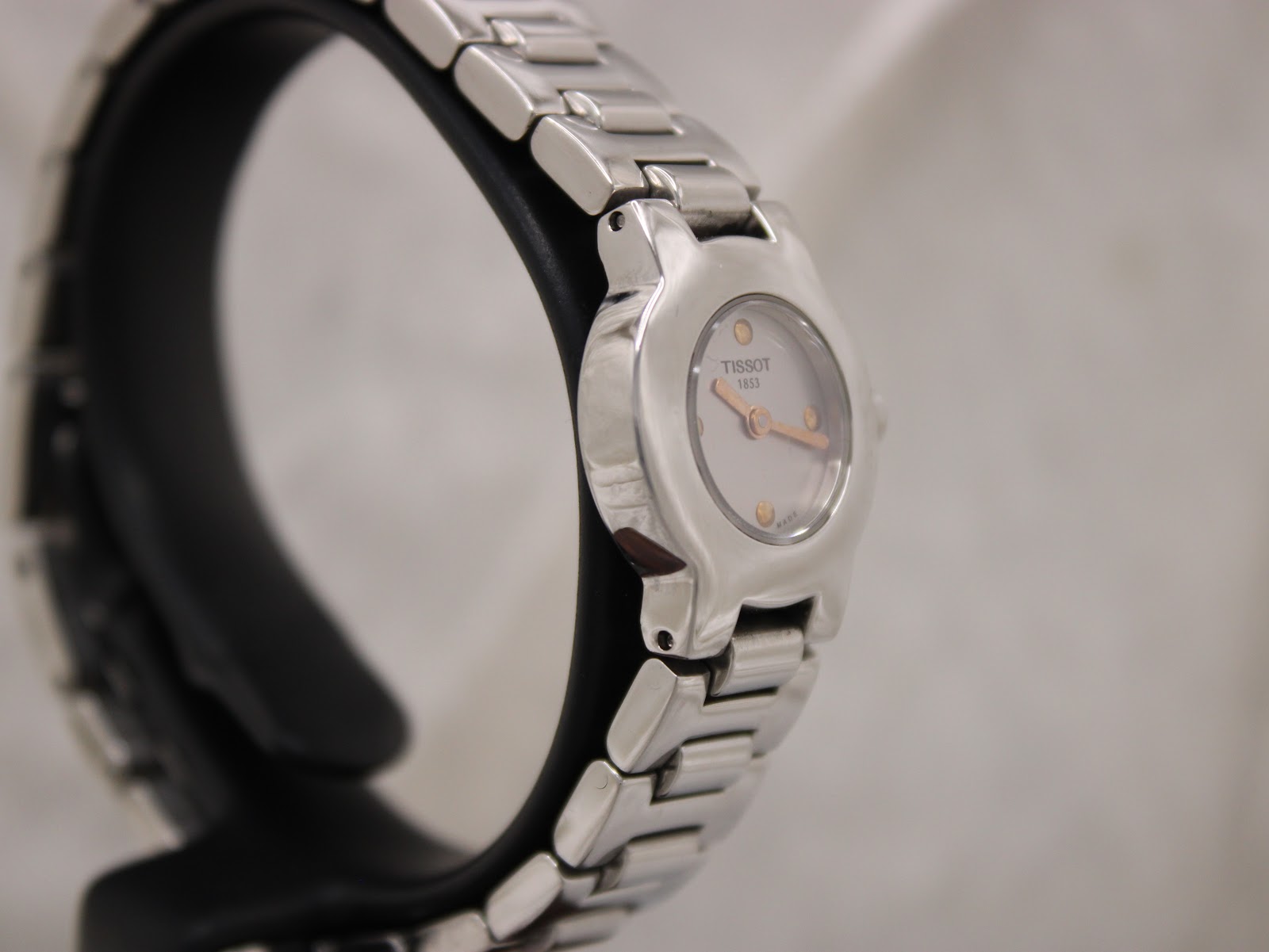Oblique side view of the Tissot watch and bracelet on a display stand, showing the dial.