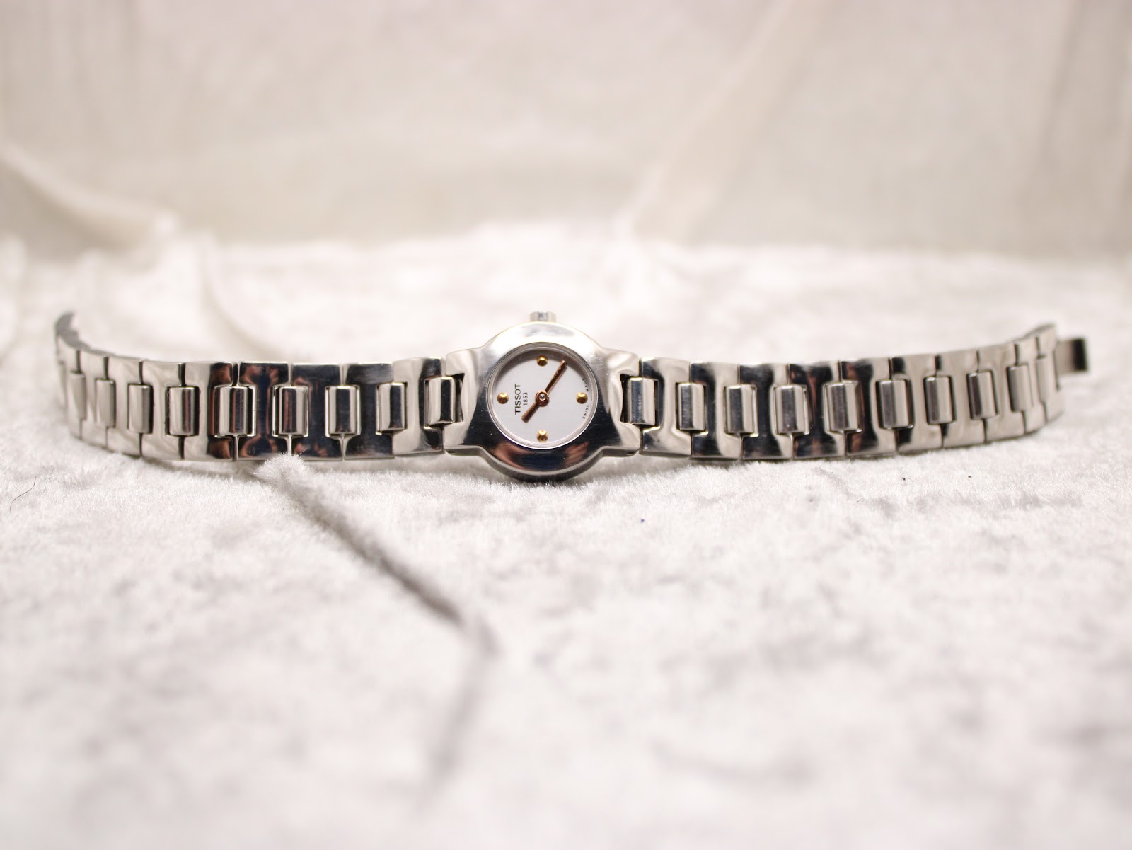 Full view of the Tissot watch and bracelet laid flat on a white textured background.