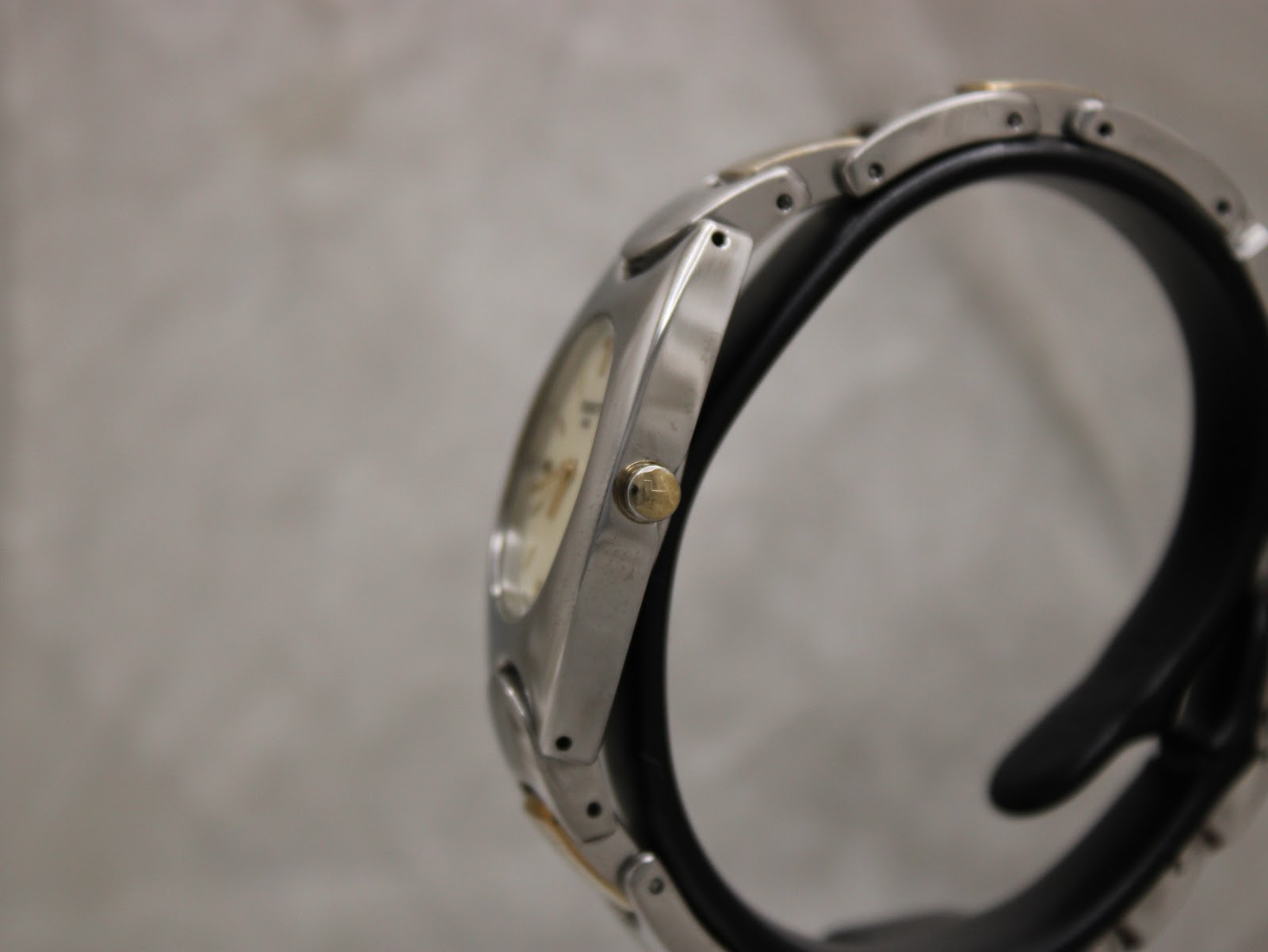 Side view of the Tissot G350 case and bracelet on a display stand, showing the gold-tone signed crown.