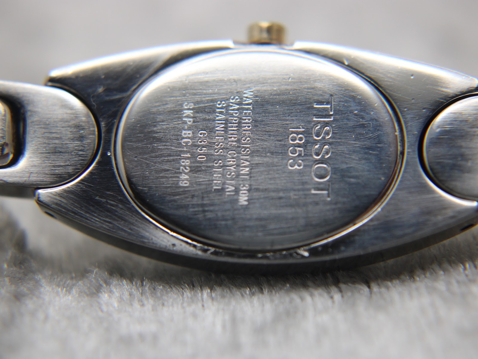 Close-up of the Tissot G350 stainless steel case back with 'Tissot 1853', 'Waterresistant 30m', 'Sapphire Crystal', 'Stainless Steel', and model/serial details engraved.