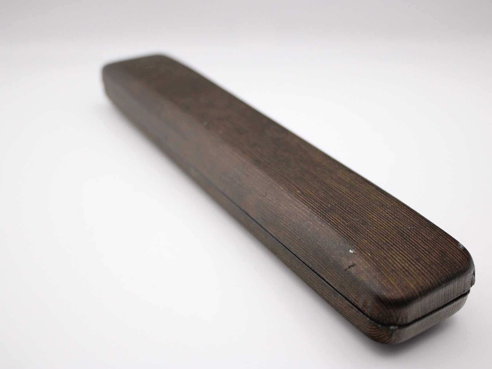 A long, slender, dark brown watch presentation box with a wood grain texture, seen from an angle.