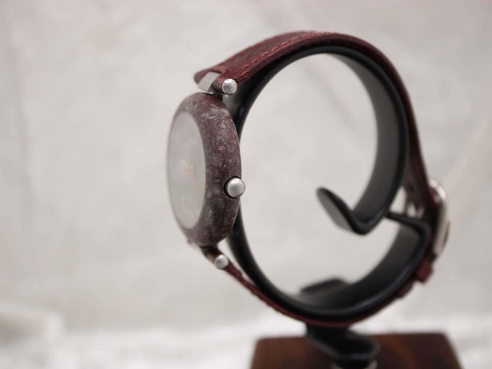 Side profile view of the Tissot RockWatch on a stand, showcasing its slim design and the natural texture of the burgundy stone case.