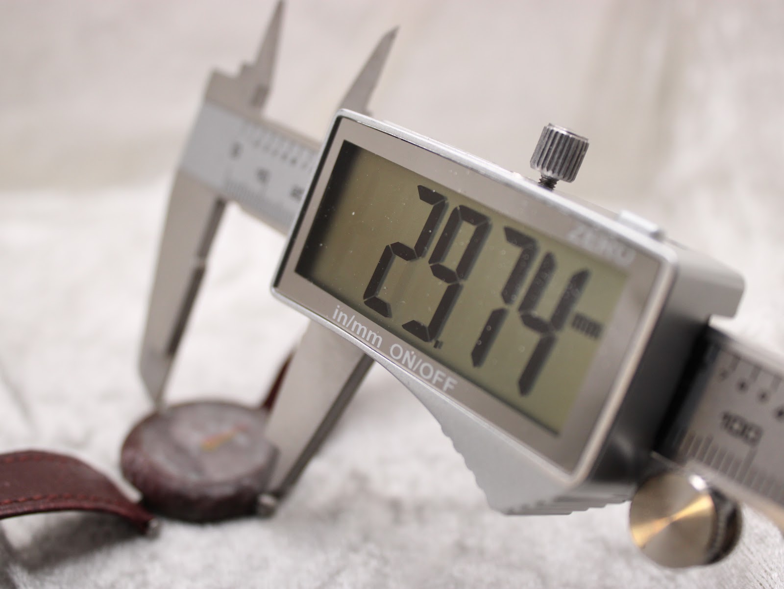 Close-up of a digital caliper measuring the watch case diameter, with the display showing 29.74 mm.