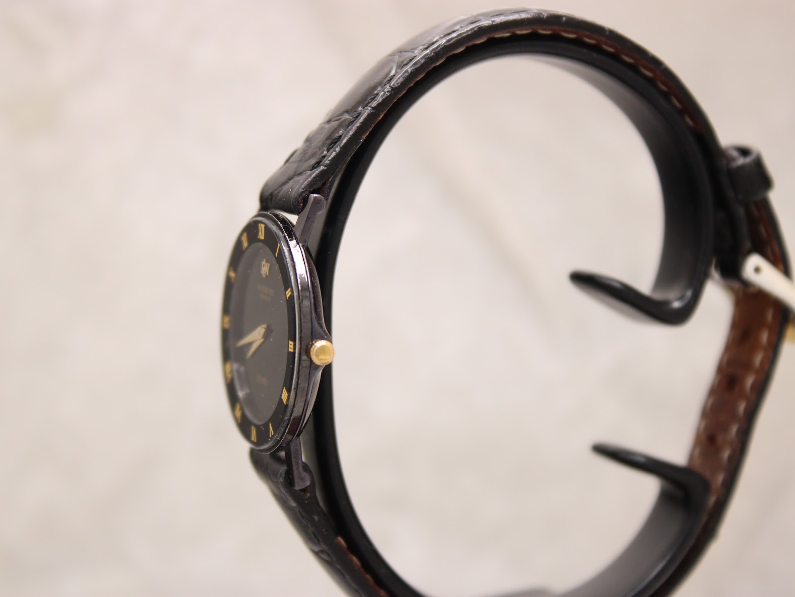 Side profile of the Raymond Weil Othello watch, highlighting its slim black-coated case and gold tone crown, displayed on a watch stand.