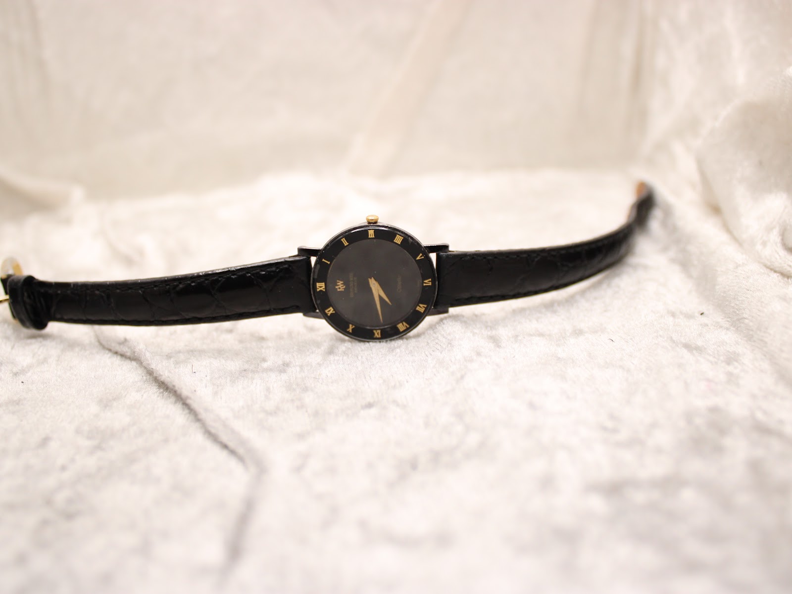 Overhead view of the Raymond Weil Othello watch, laid flat to display the full length of the black leather strap and its gold tone buckle.