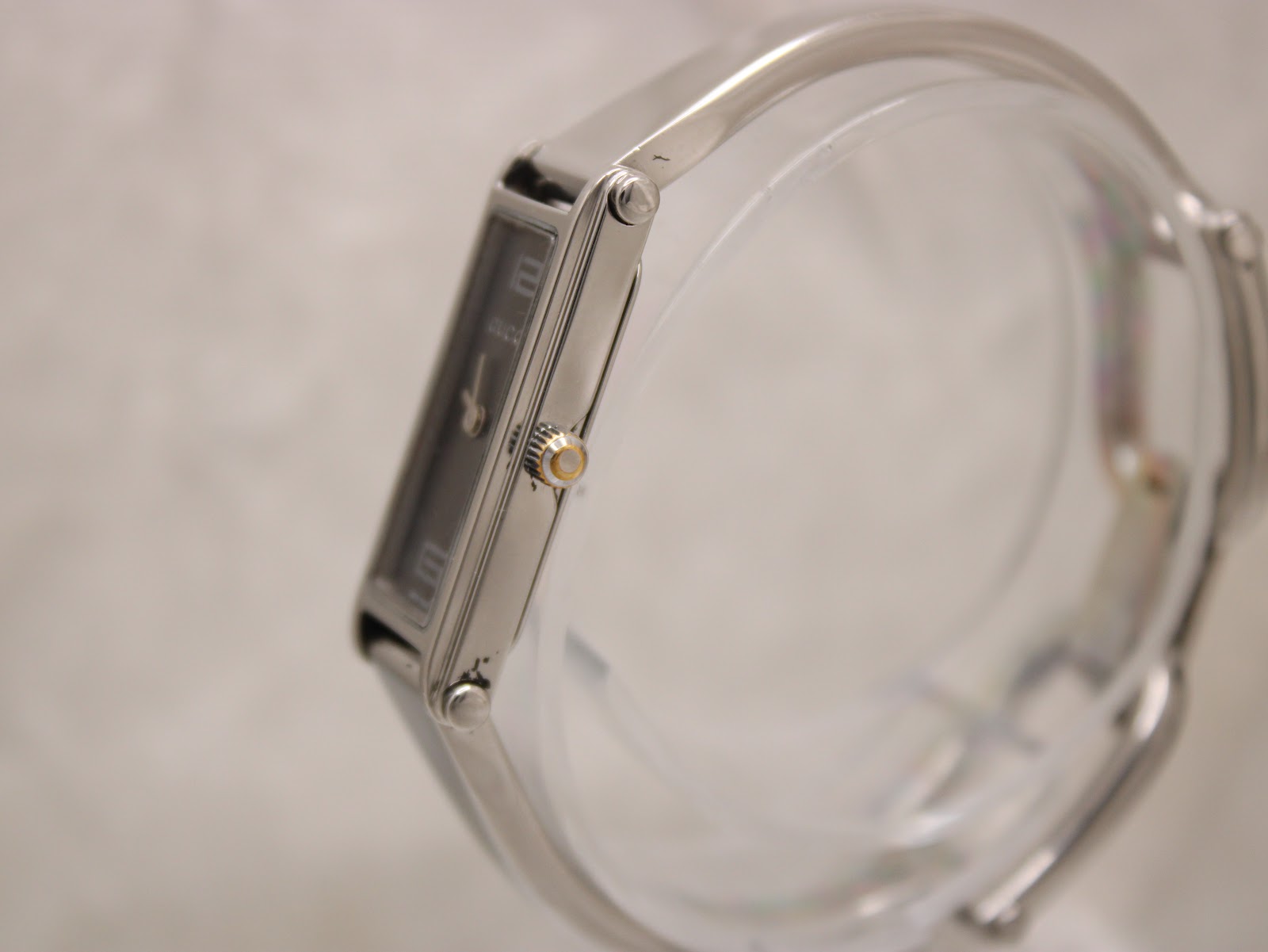 Side view of the Gucci 1500L watch case and crown on a clear stand.