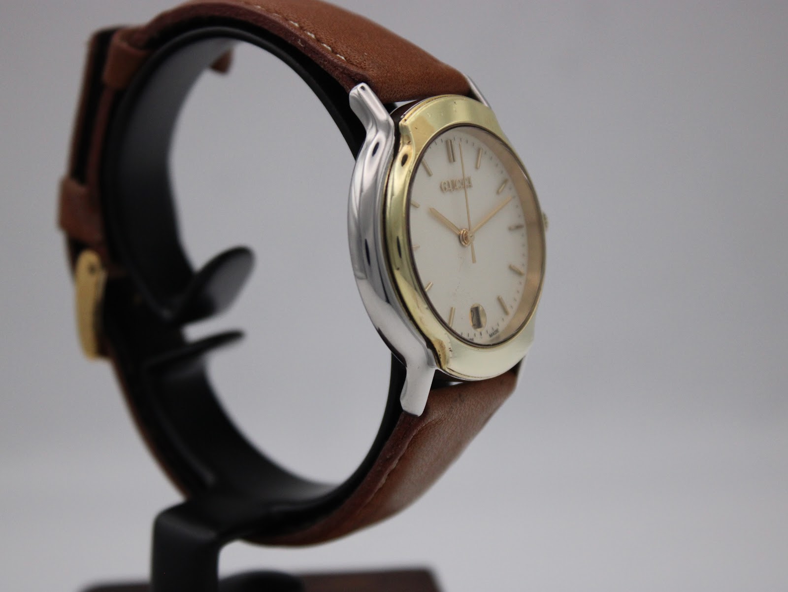 Angled side view of the Gucci watch on a display stand, highlighting the case and strap.