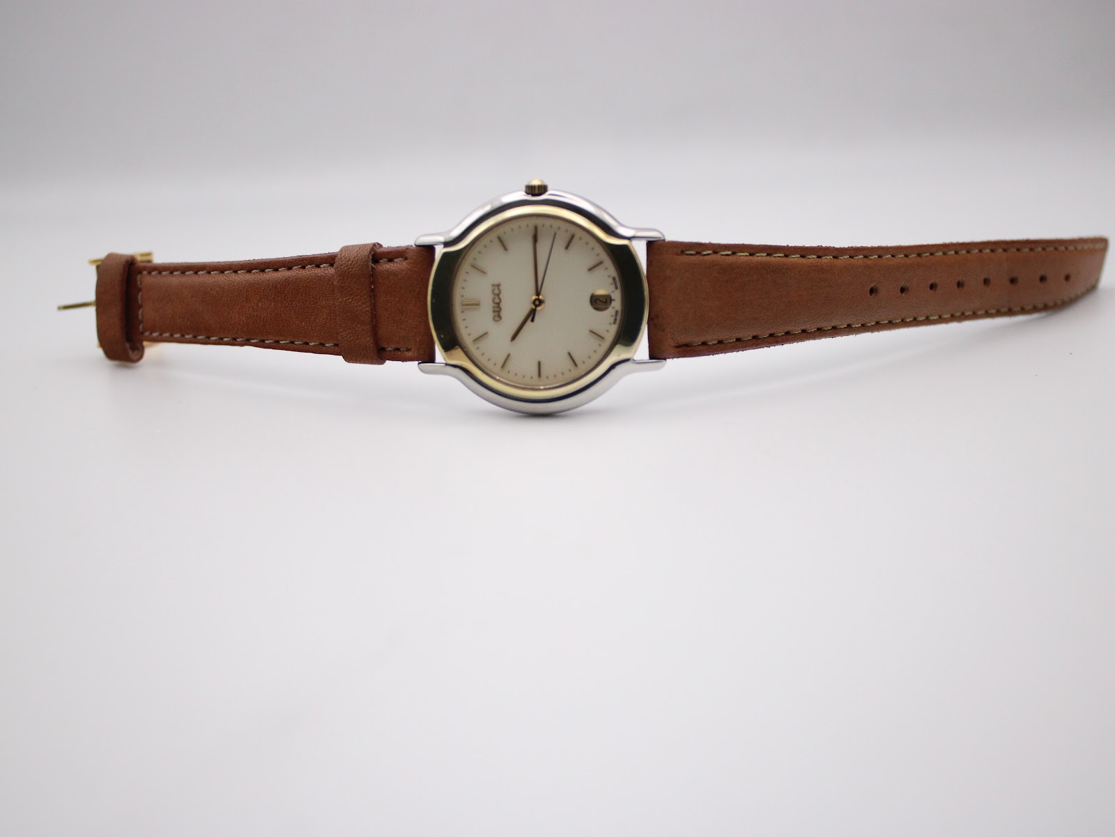 Full length view of the Gucci watch laid flat, showing the brown leather strap and gold-tone buckle.