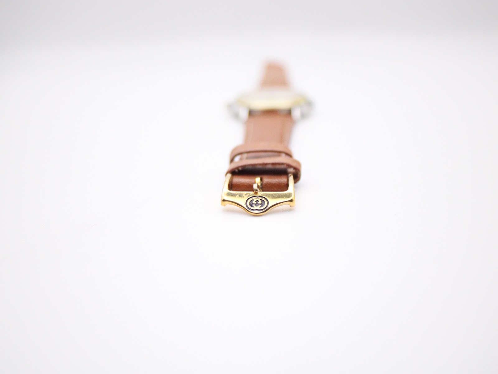 Close-up of the original Gucci-signed gold-tone buckle on the brown leather strap.