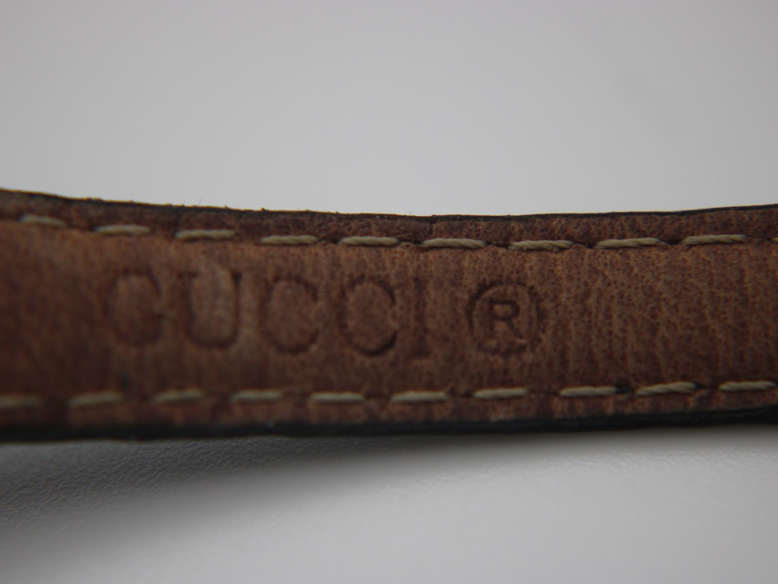Close-up of the embossed 'GUCCI' logo on the brown underside of the black leather watch strap.