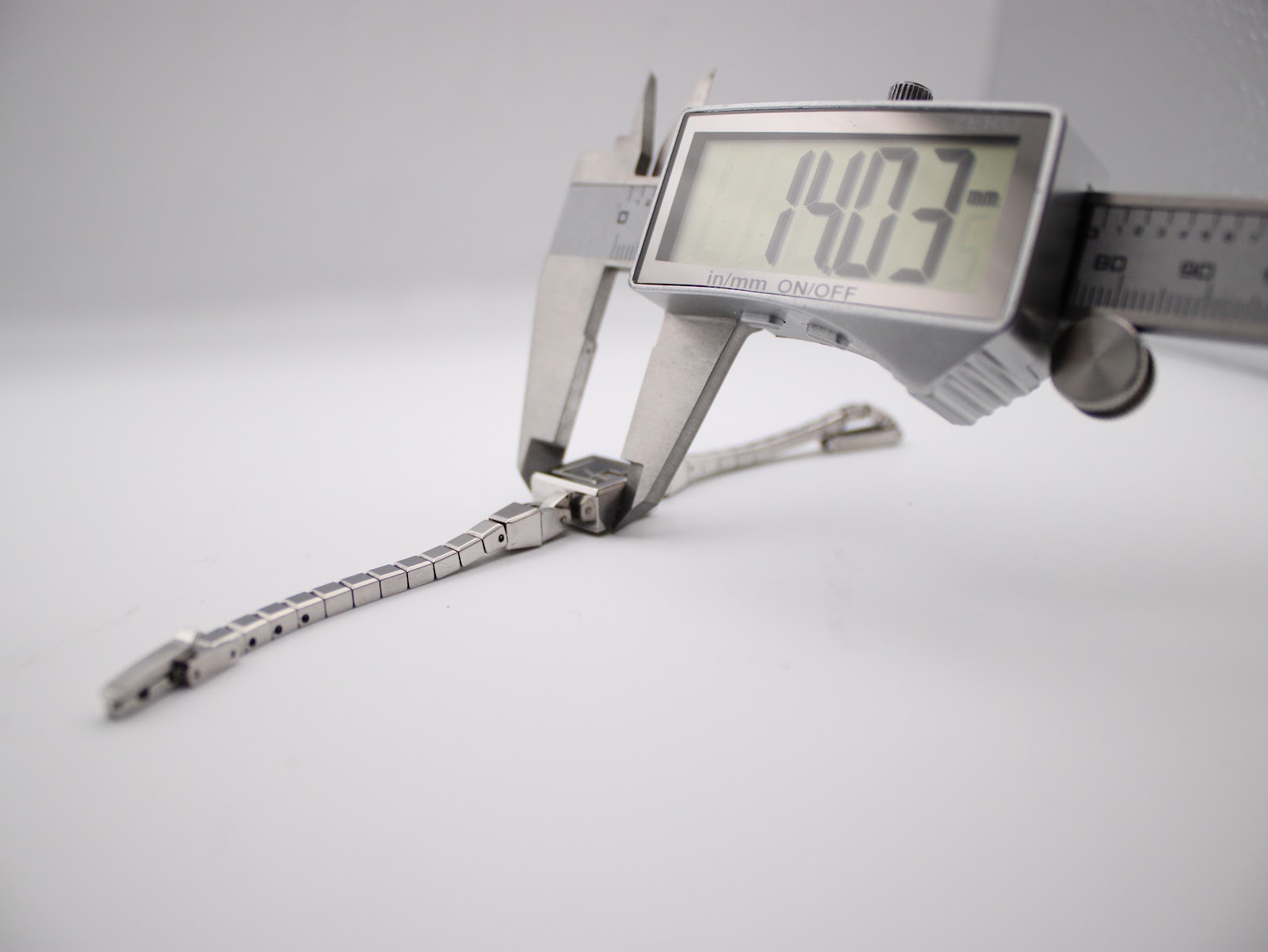 Digital caliper measuring the case diameter of the Gucci G-Frame watch, showing a precise measurement of 14.03 mm.