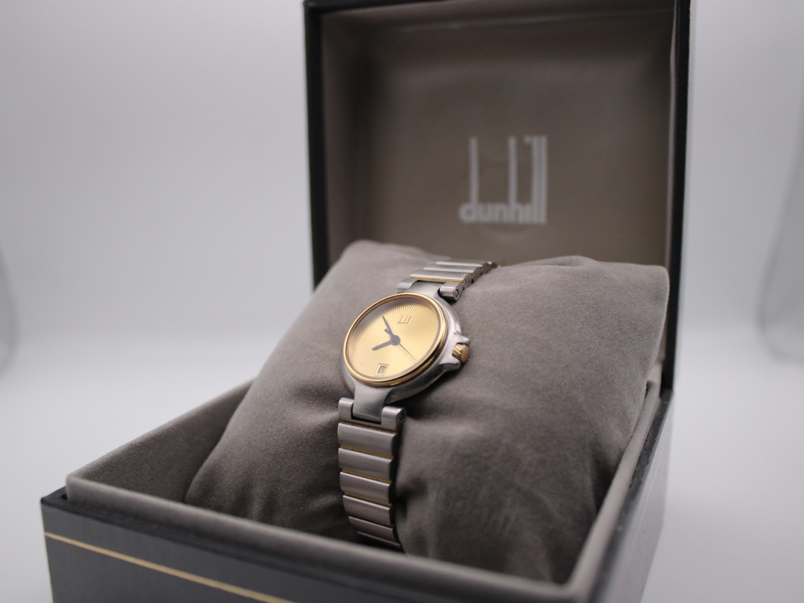 Dunhill watch presented in its original black box with gold trim, resting on a grey cushion.