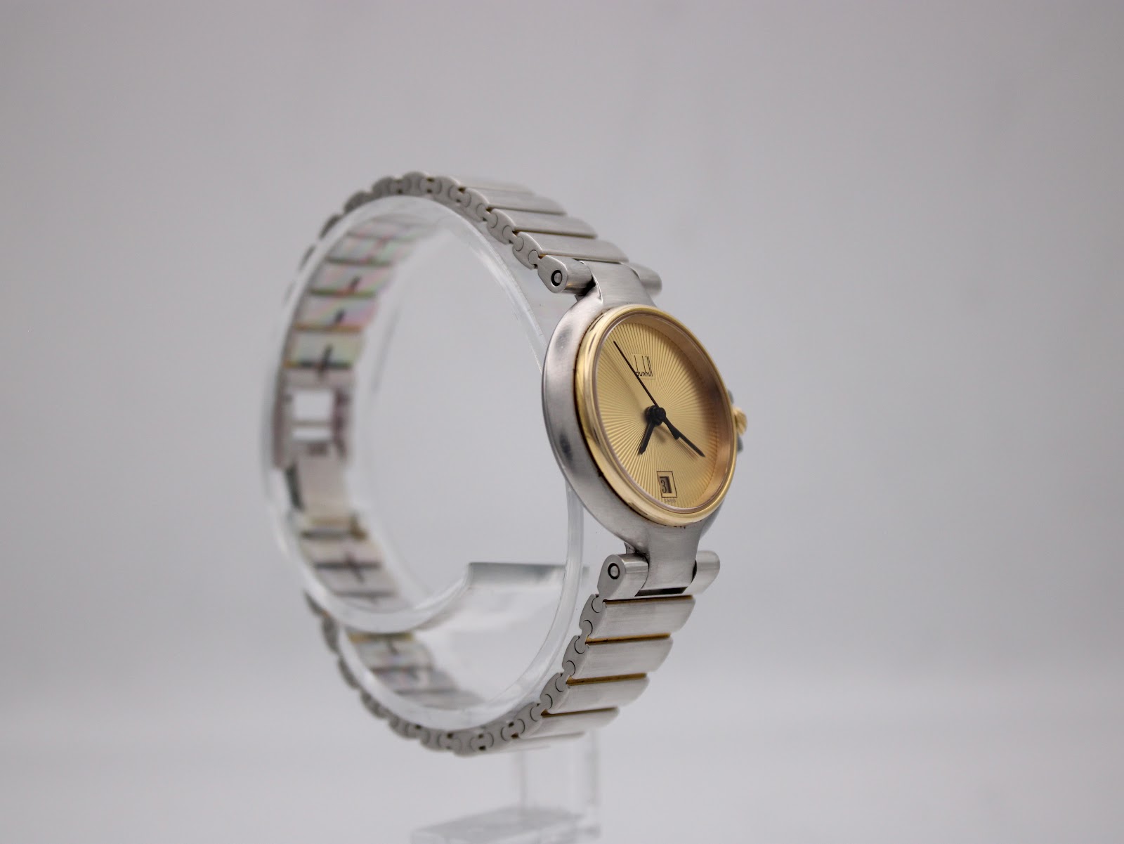 Other angled side view of the Dunhill watch on a clear stand, highlighting case profile and two-tone bracelet.