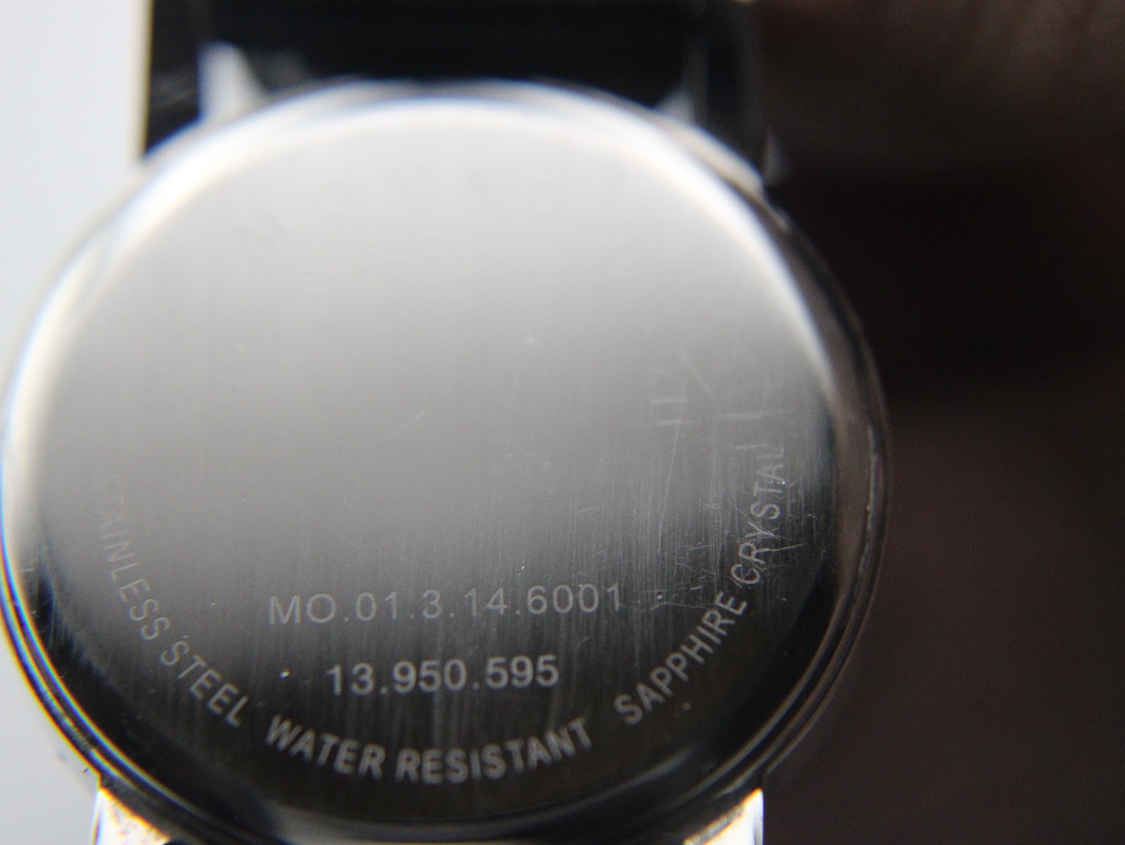 Close-up of the polished stainless steel case back, showing engraved reference number MO.01.3.14.6001 and 'water resistant sapphire crystal' text.