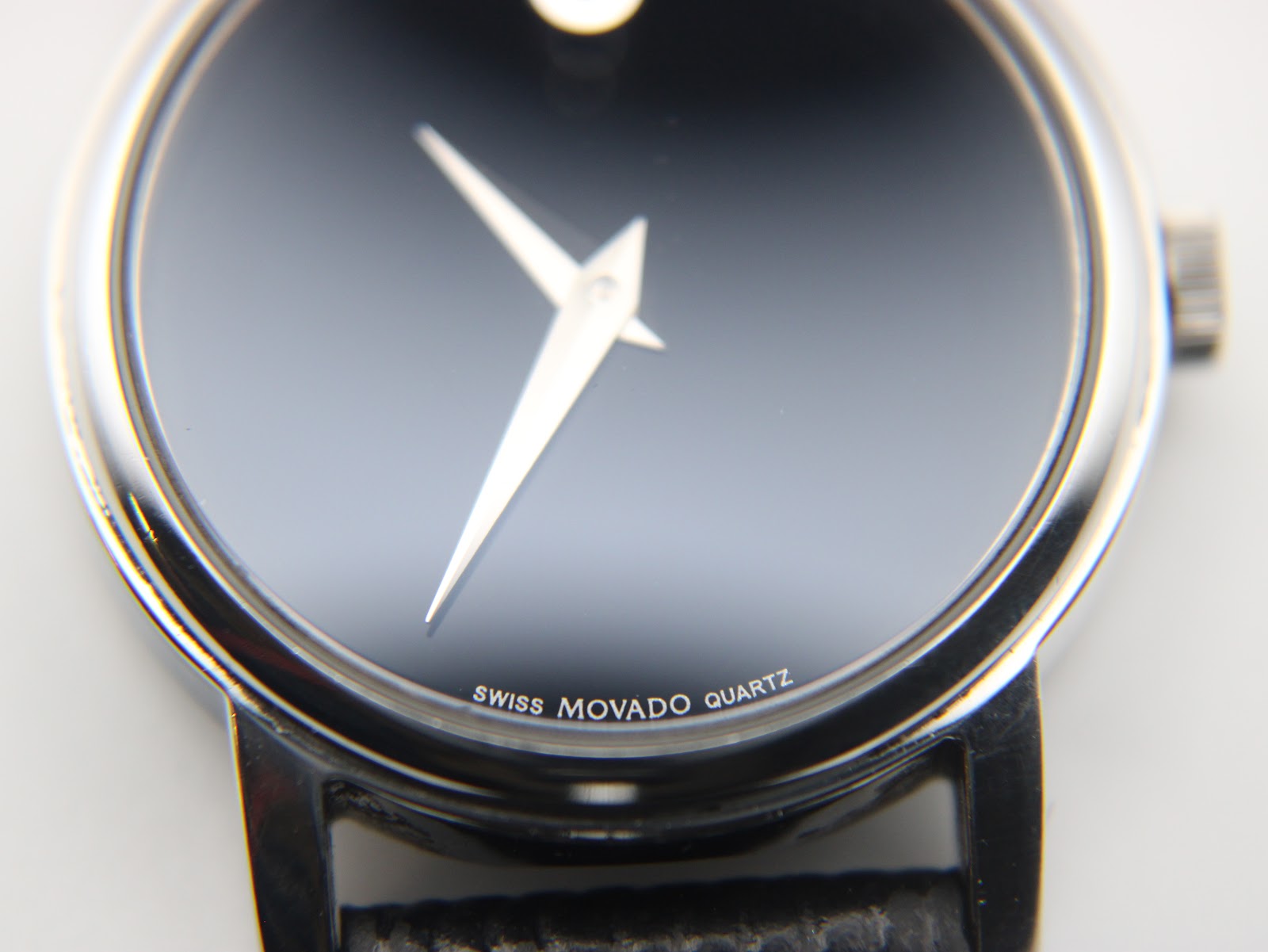 Extreme close-up of the black museum dial, showing the iconic silver dot at 12 o'clock and subtle 'swiss movado quartz' text at 6 o'clock.