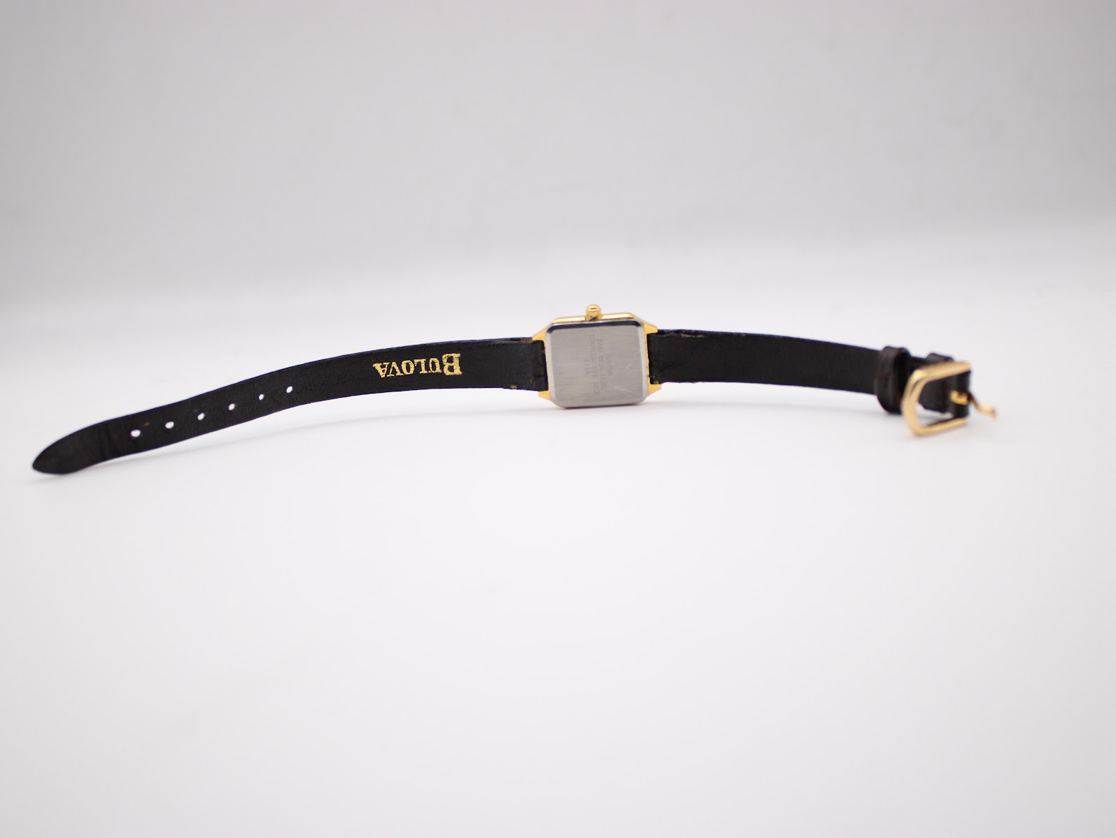 Back view of the Bulova watch with the strap laid flat, showing 'Bulova' embossed on the strap and the stainless steel case back.