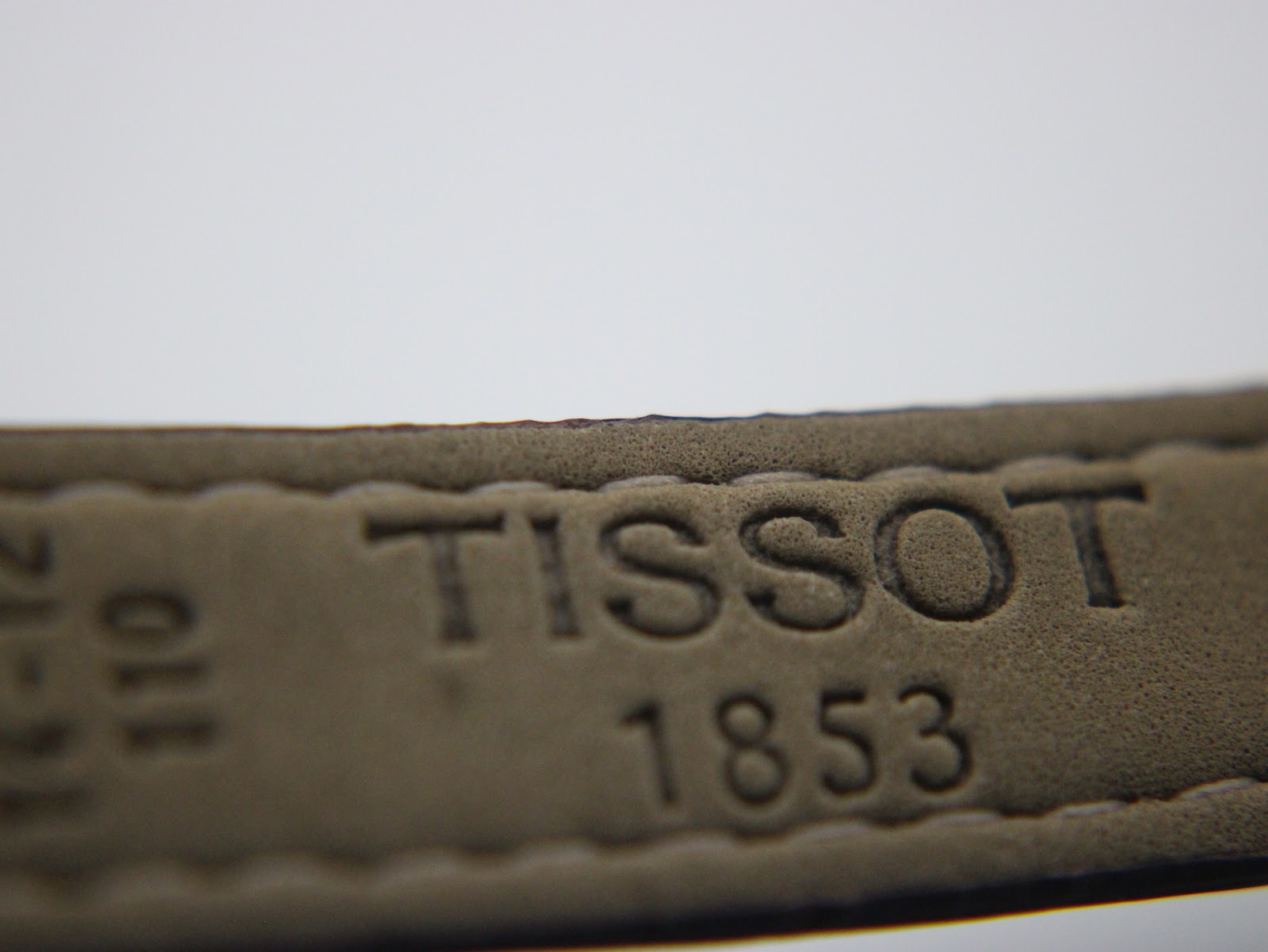 Close-up of the underside of the dark brown leather strap with "TISSOT 1853" embossed.