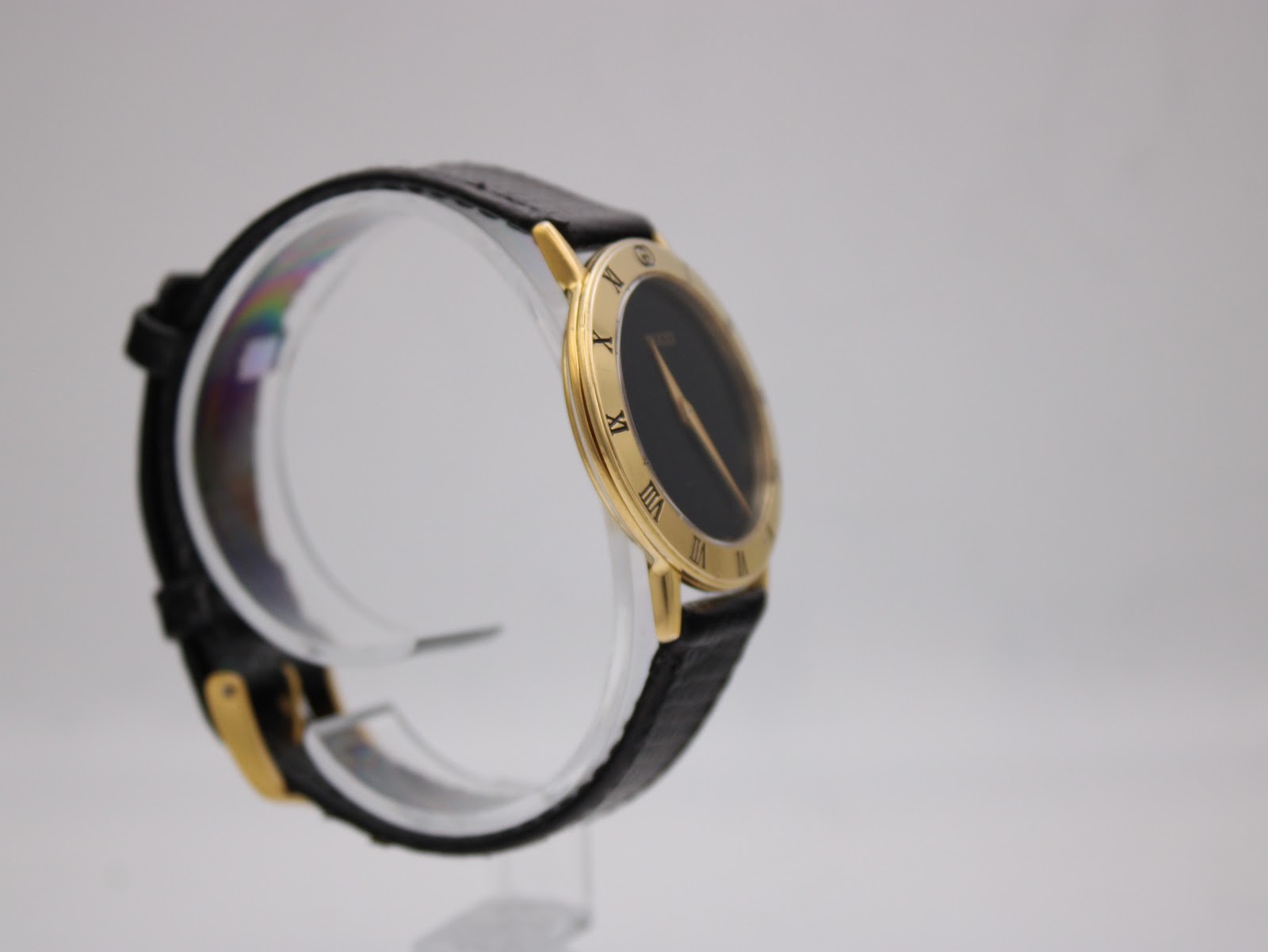 Opposite angled side view of the Gucci 3000.2.M watch, highlighting the case profile and black leather strap on a clear display stand.