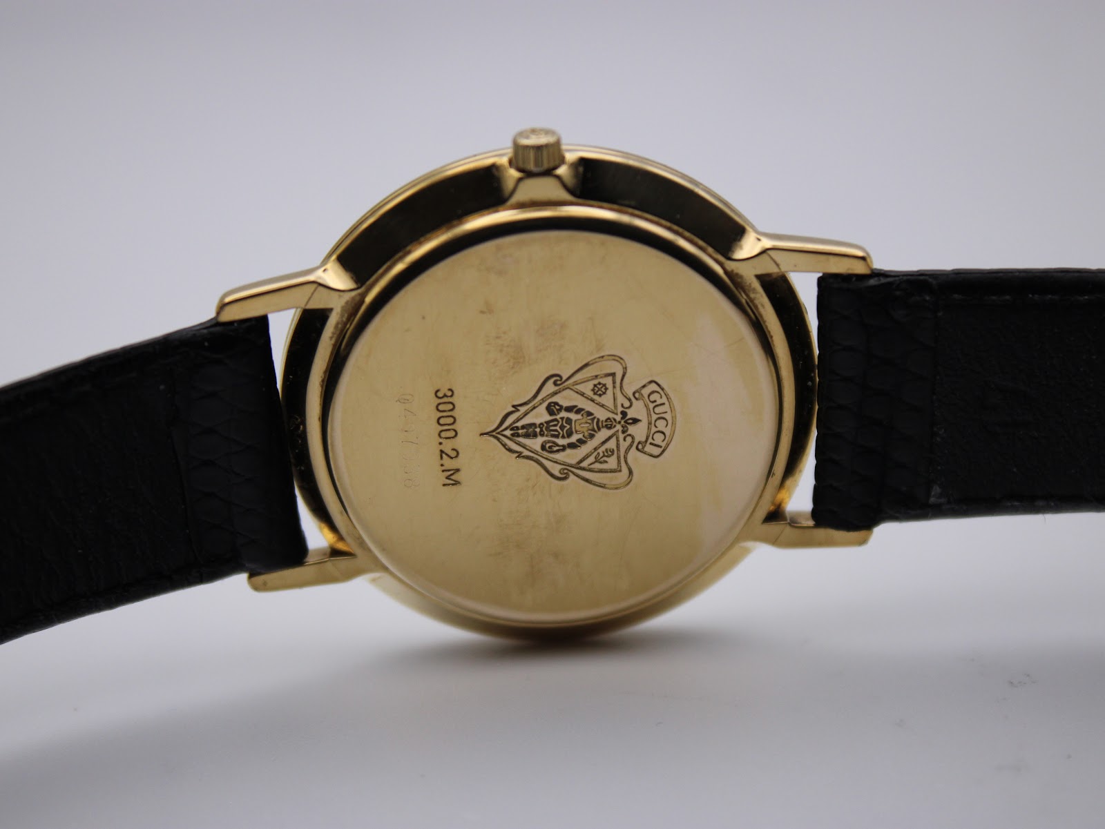 Close-up of the watch's gold-tone case back, showing the model number '3000.2.M' and the engraved Gucci crest.