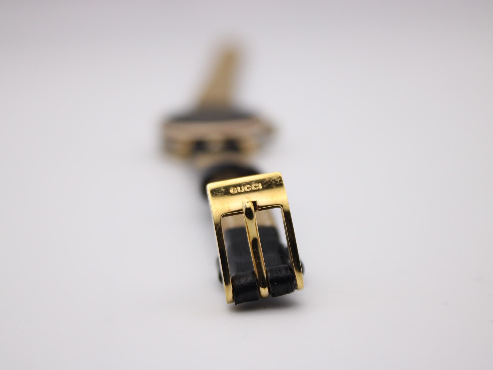 Close-up of the gold-tone buckle on the black leather strap, clearly showing the 'GUCCI' engraving.
