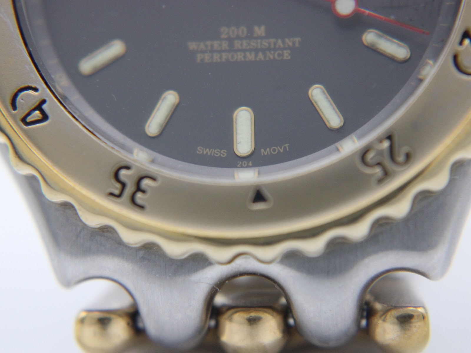 Macro close-up of the black dial showing 'swiss movt' text, luminous hour markers, and '200 M water resistant performance' text.