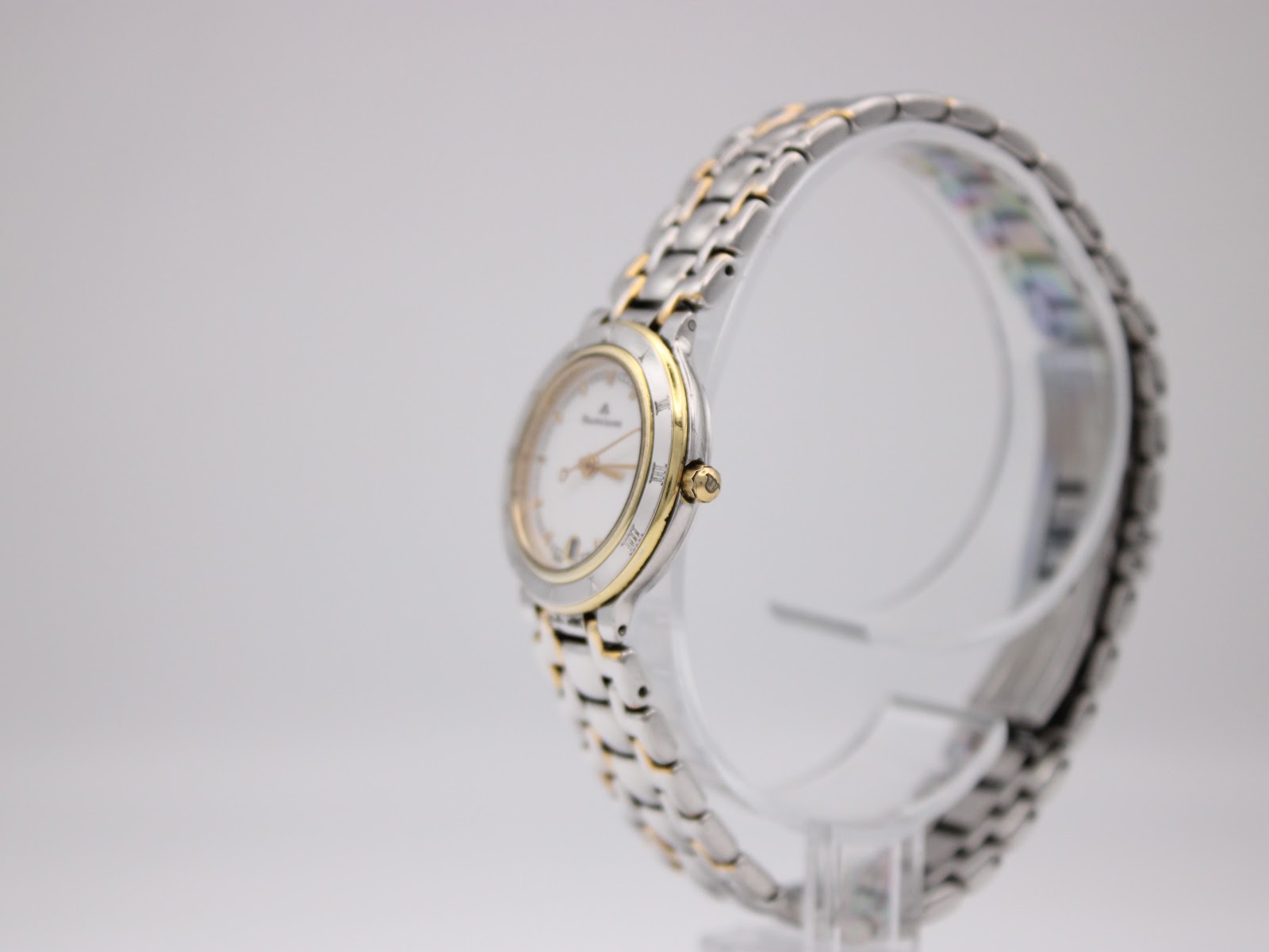 Side view of the Maurice Lacroix watch on a display stand, showing the gold-tone crown and the two-tone bracelet.