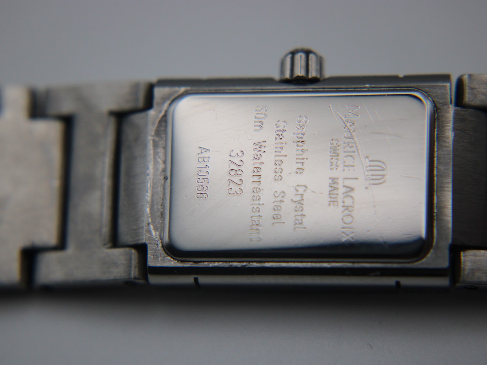 Close-up of the polished stainless steel case back, showing Maurice Lacroix, Swiss Made, sapphire crystal, stainless steel, 50m water resistant, model 32823, and serial AB10566 engravings.