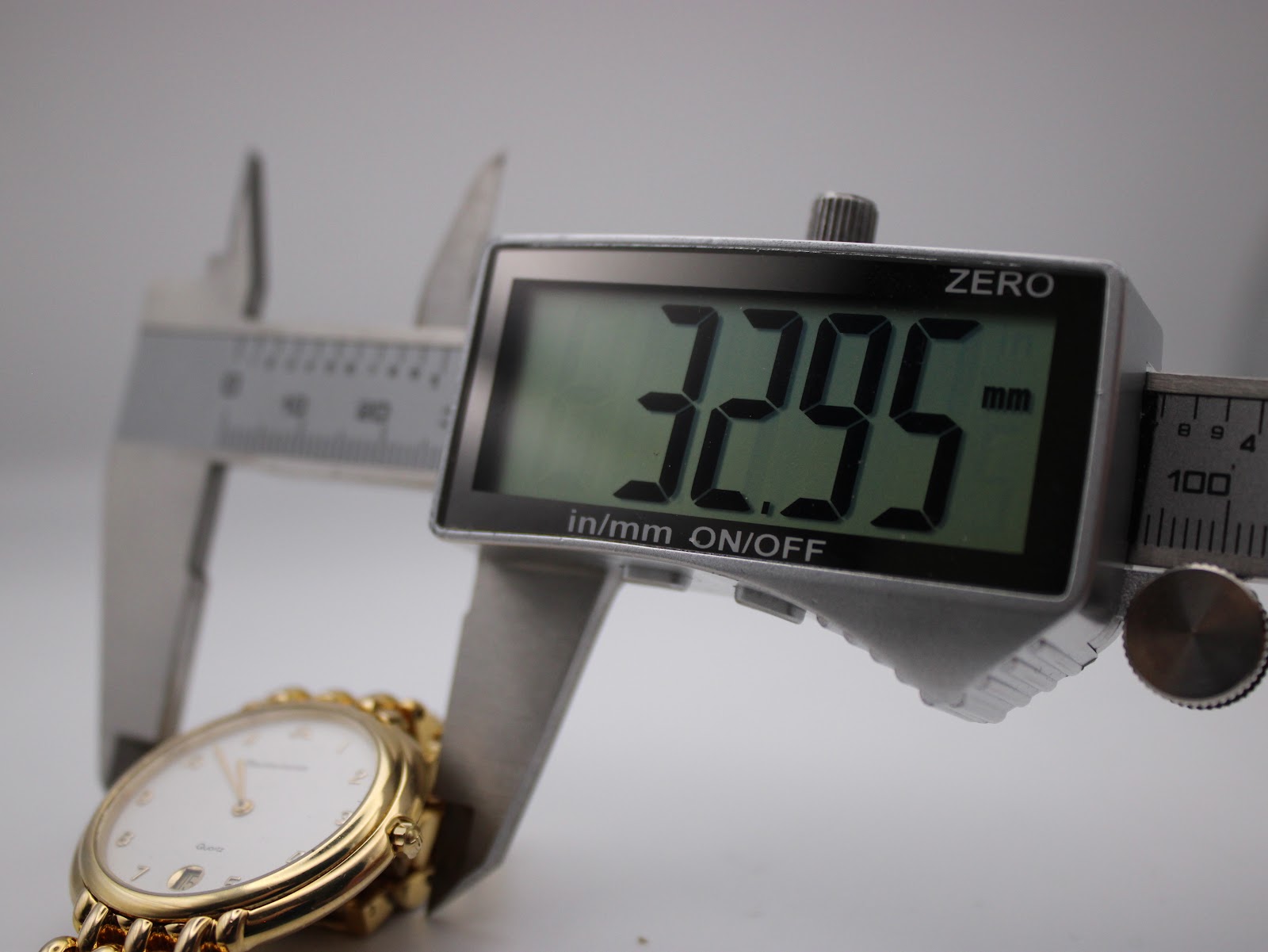Digital caliper measuring the case diameter of the watch, displaying '32.95 mm'.