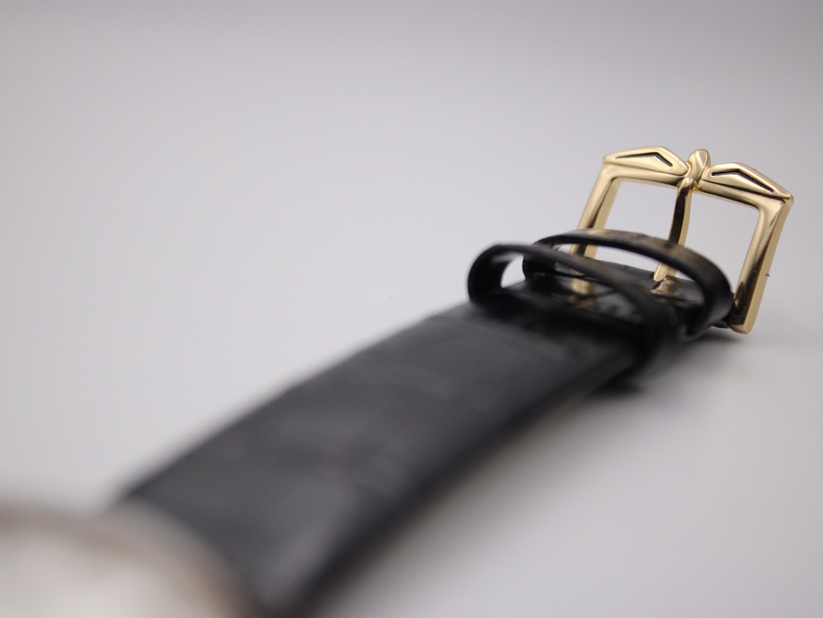 Close-up of the gold-tone pin buckle on the black leather strap, featuring a classic, elegant design.