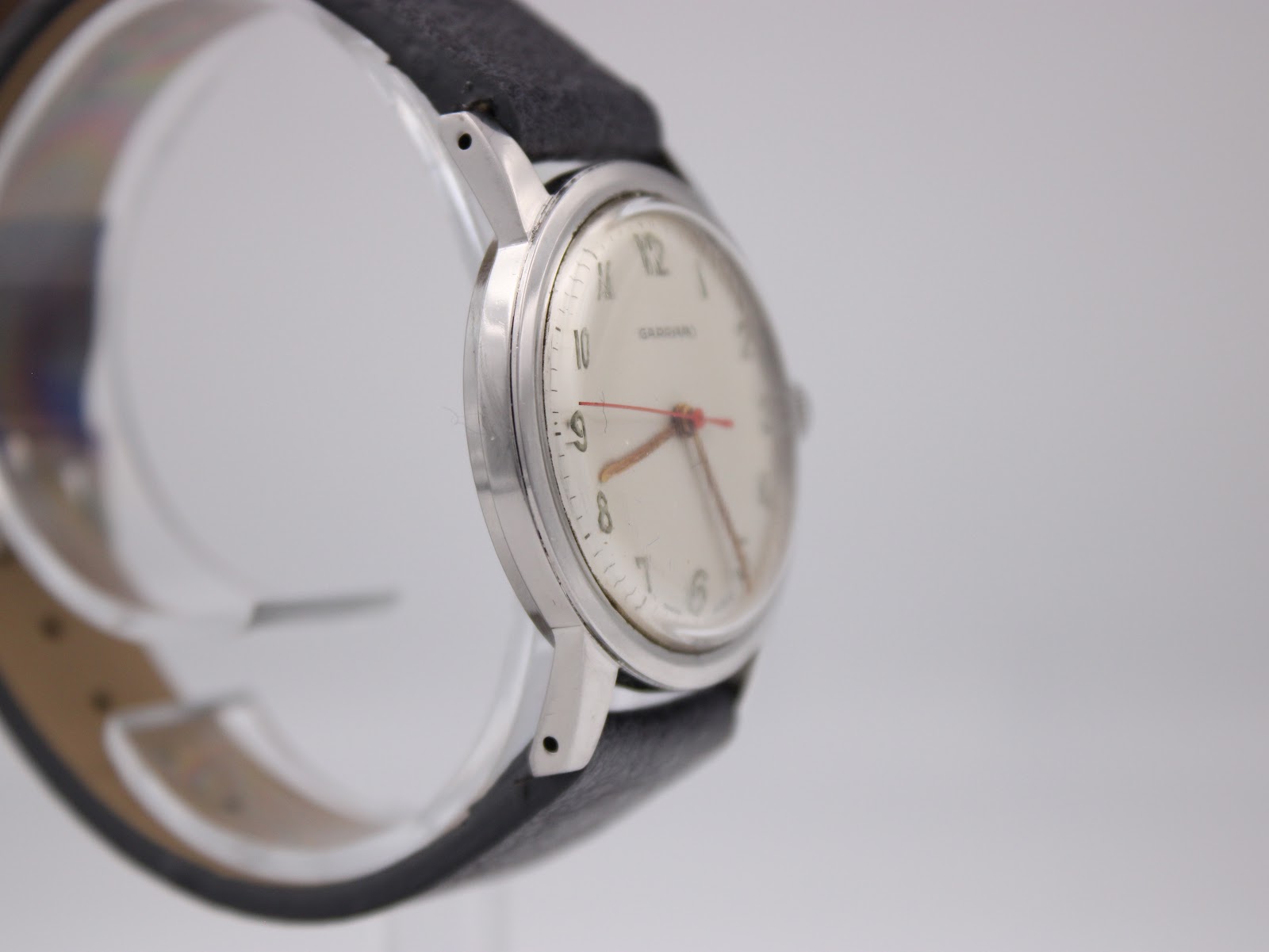 Angled side view of the Garrard watch, highlighting the lugs, case shape, and texture of the grey leather strap.