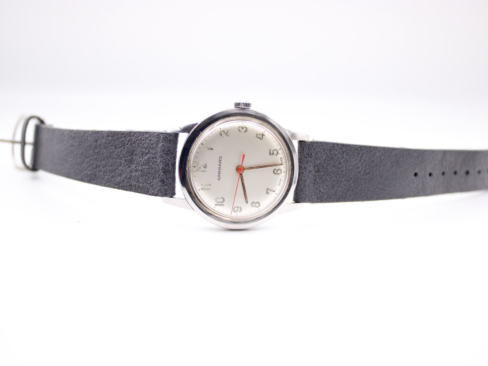 Full length view of the Garrard watch with its grey leather strap laid flat on a white background.