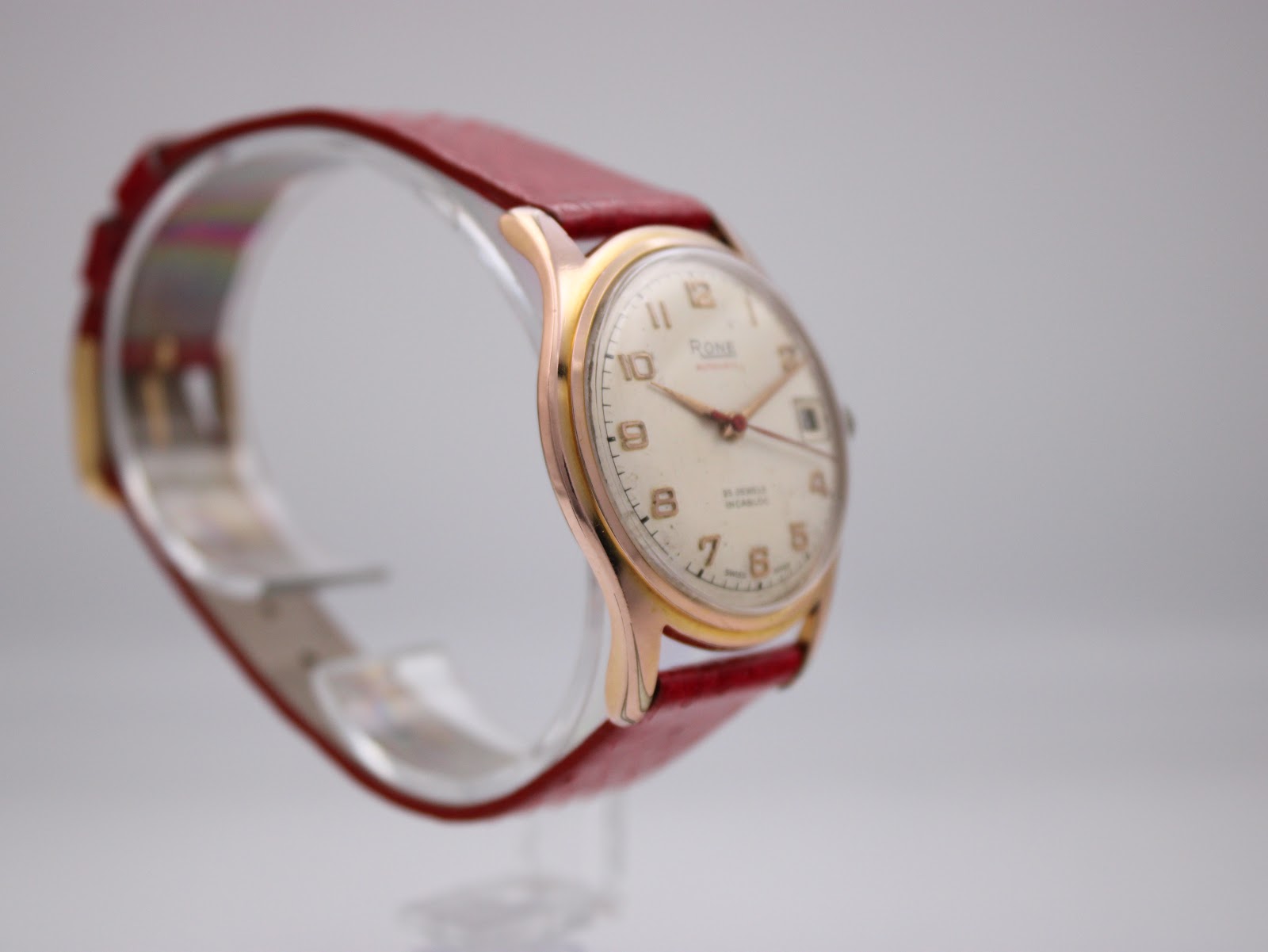 Angled side view of the Rone watch on a clear stand, showcasing the elegant lugs and gold-tone finish of the case.
