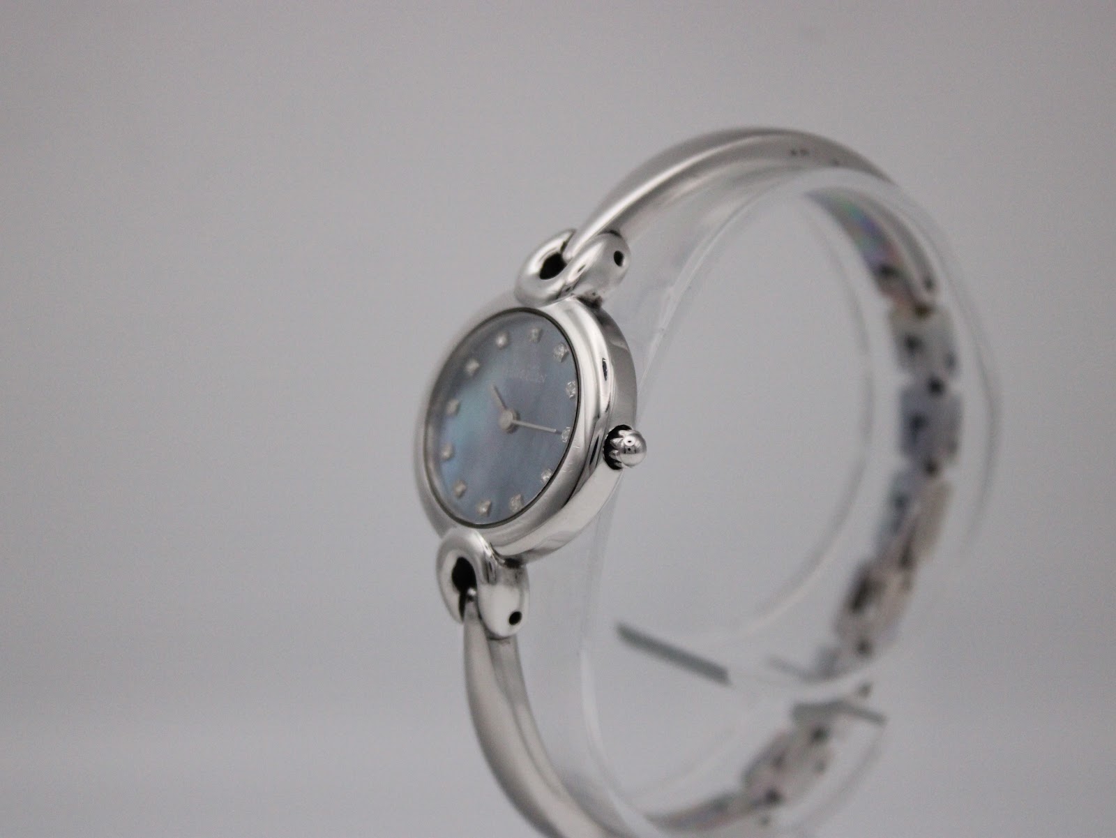 Side view of the Michel Herbelin watch on a clear stand, showing the case profile and integrated bangle bracelet.