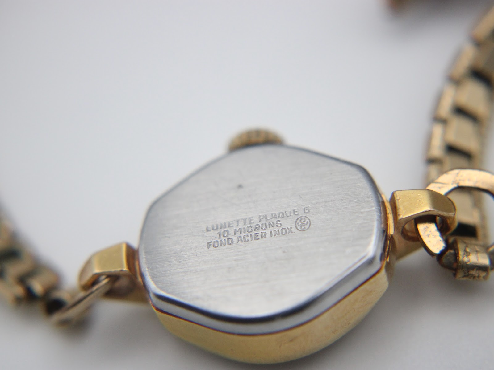 View of the watch case back, engraved "Lunette Plaqué G 10 Microns / Fond Acier Inox."