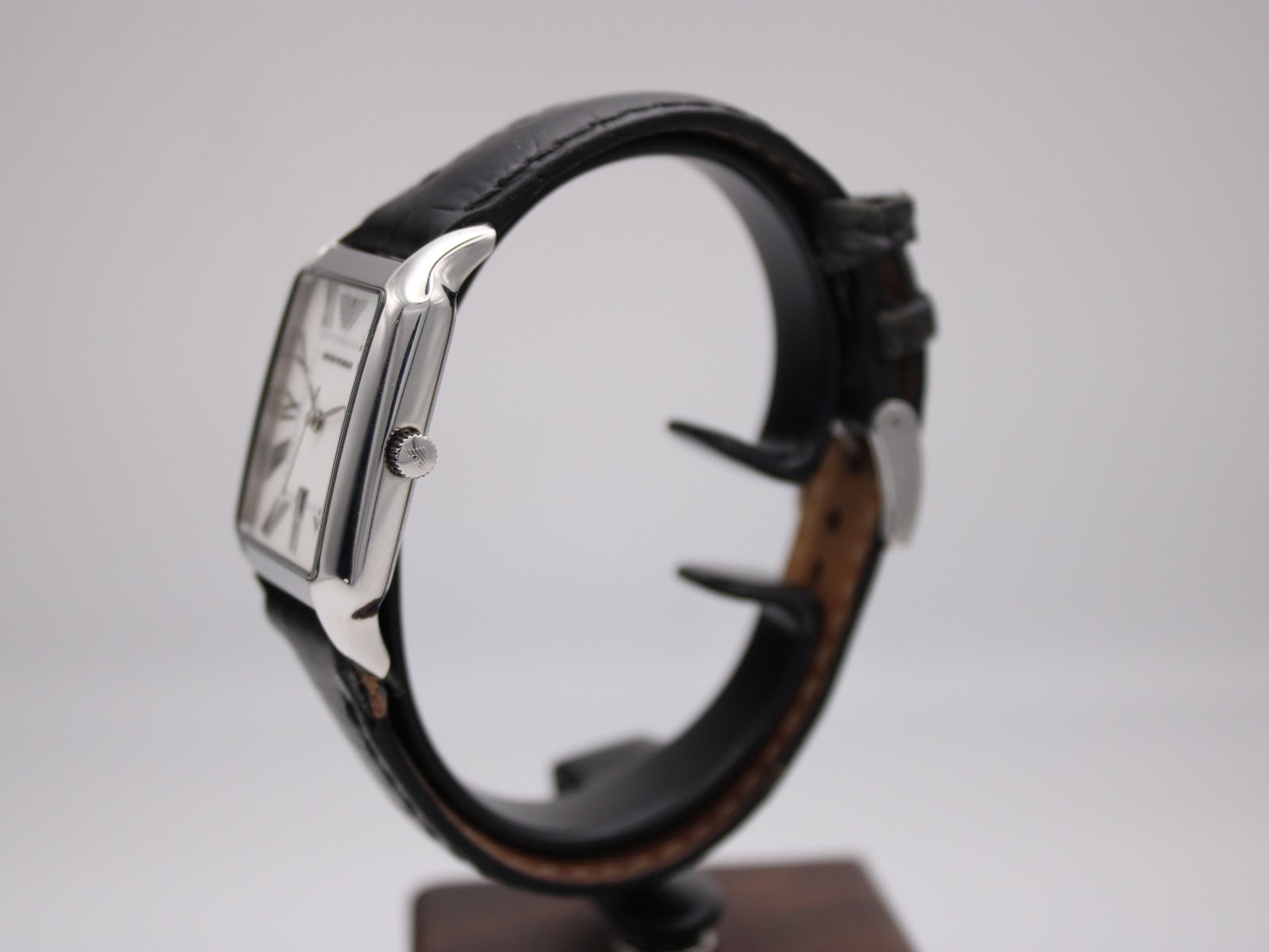 Side profile view of the Emporio Armani AR-0413 watch on a stand, highlighting the polished stainless steel case and crown.