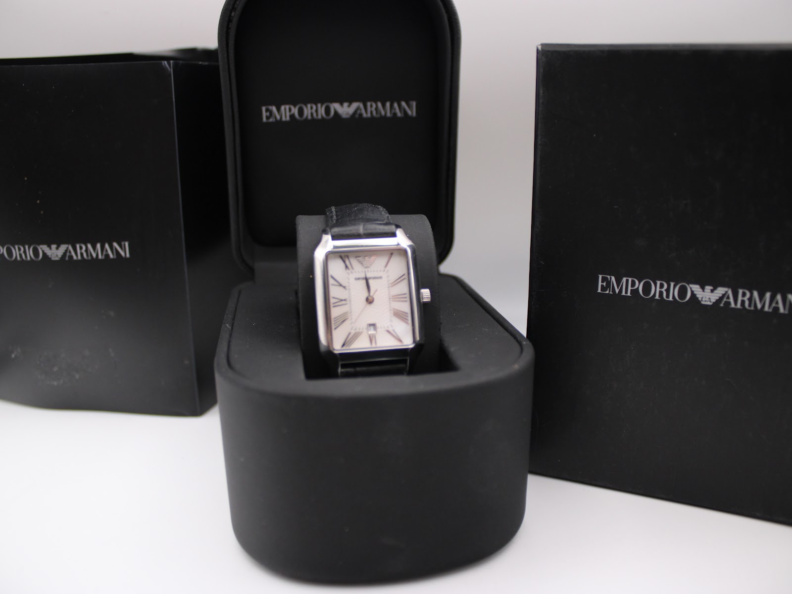 The Emporio Armani AR-0413 watch presented inside its original black Emporio Armani branded presentation box, with outer boxes in the background.