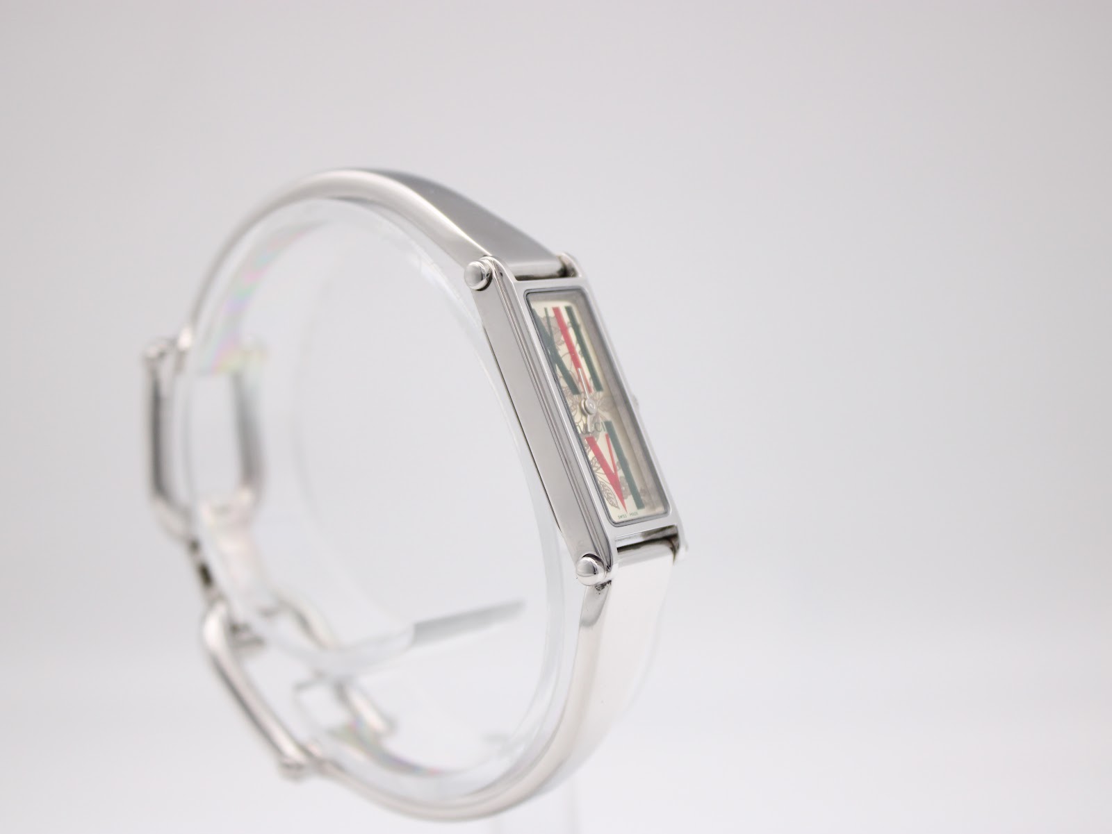 Left-side view of the Gucci 1500L watch on a display stand, showcasing the sleek lines of the stainless steel bangle bracelet and case.