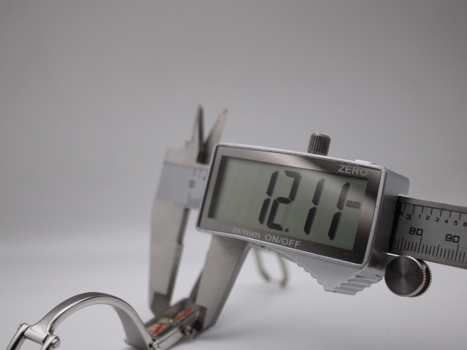 Close-up shot showing callipers measuring the width of the Gucci 1500L watch case, displaying "12.11 mm" on the digital screen.