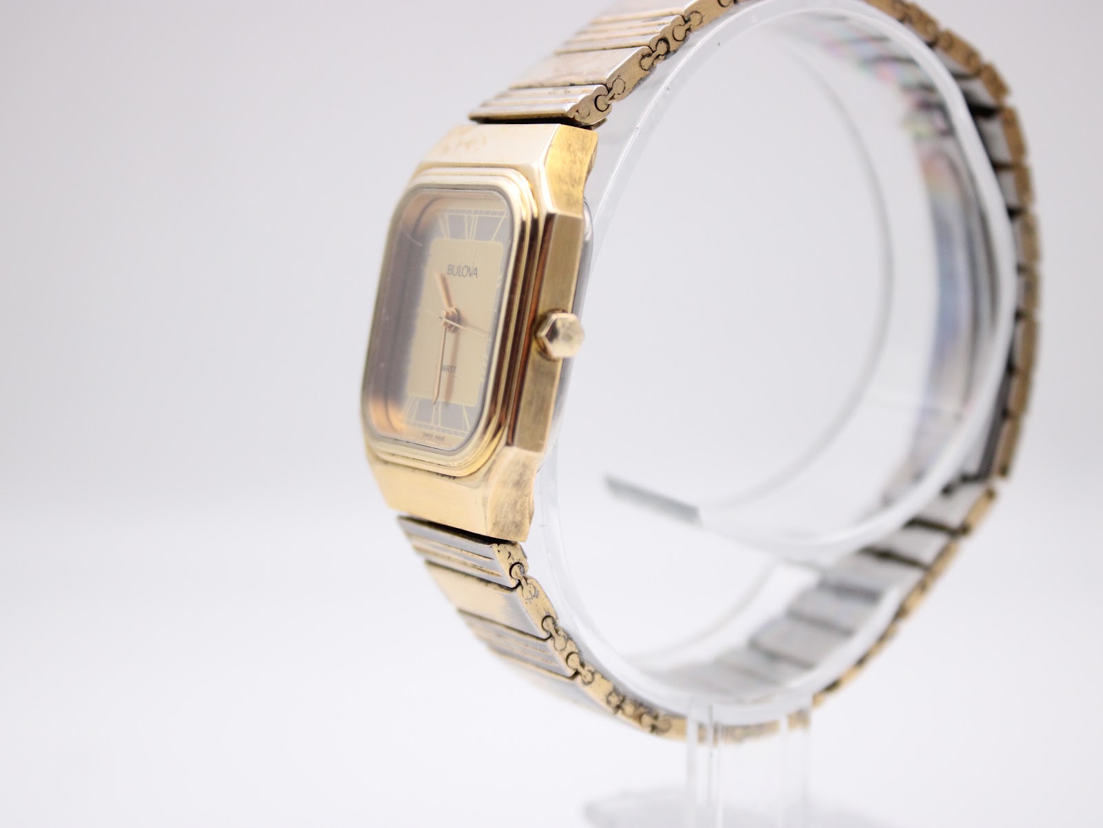 Side profile view of the gold tone Bulova P2 watch and integrated bracelet on a clear display stand.