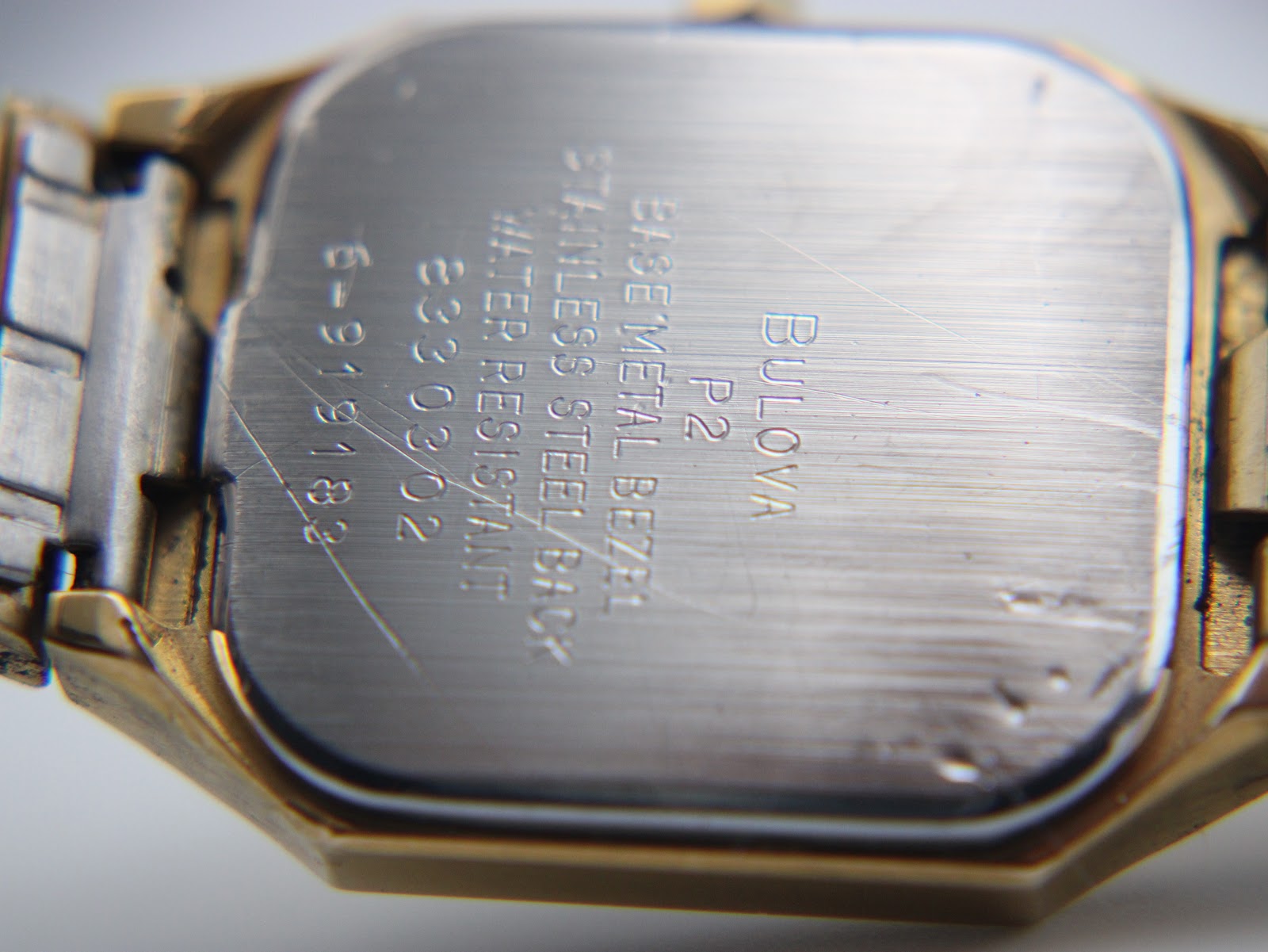 Close-up of the stainless steel case back, engraved with "Bulova P2", "Base Metal Bezel", "Stainless Steel Back", "Water Resistant", and serial number.