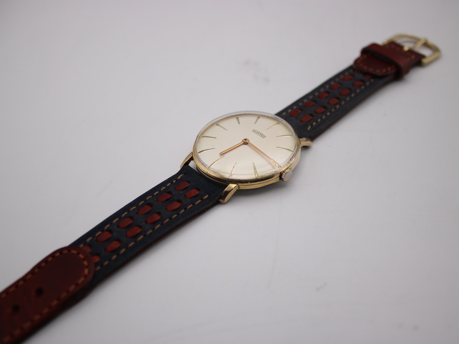 Full view of the Roamer watch on a display stand, presenting the entire length of its two-tone perforated leather strap.