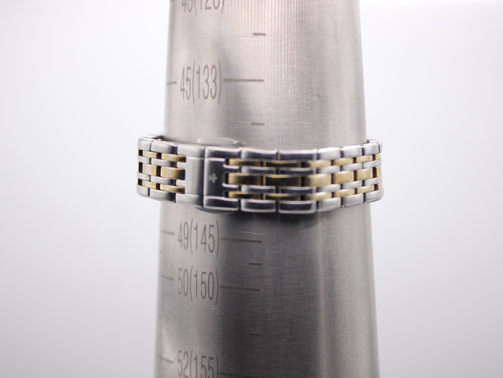 The two-tone bracelet on a wrist sizing cone, showing a circumference of approximately 145mm.