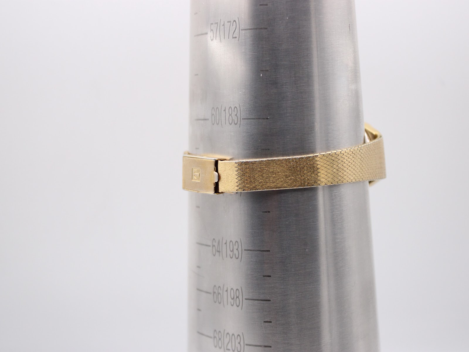 The integrated gold-tone bracelet shown on a wrist sizing gauge, indicating a wrist size of approximately 16.2cm.